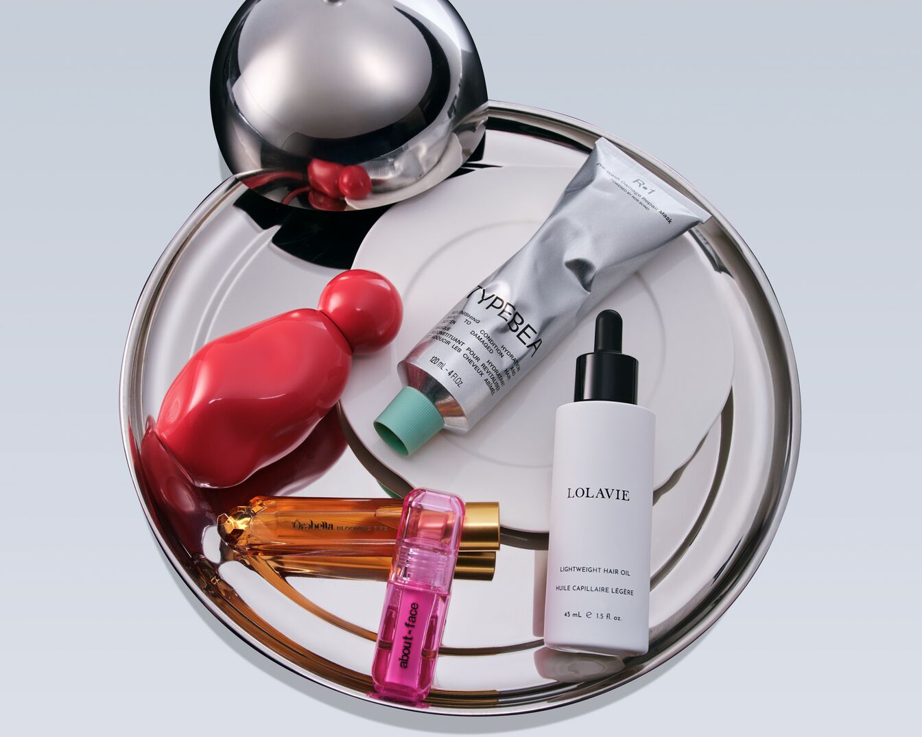 Découvrez une sélection de produits de beauté : parfum rouge vif, soin capillaire TYPEBEA en tube argenté, huile légère LOLAVIE et gloss about-face rose.