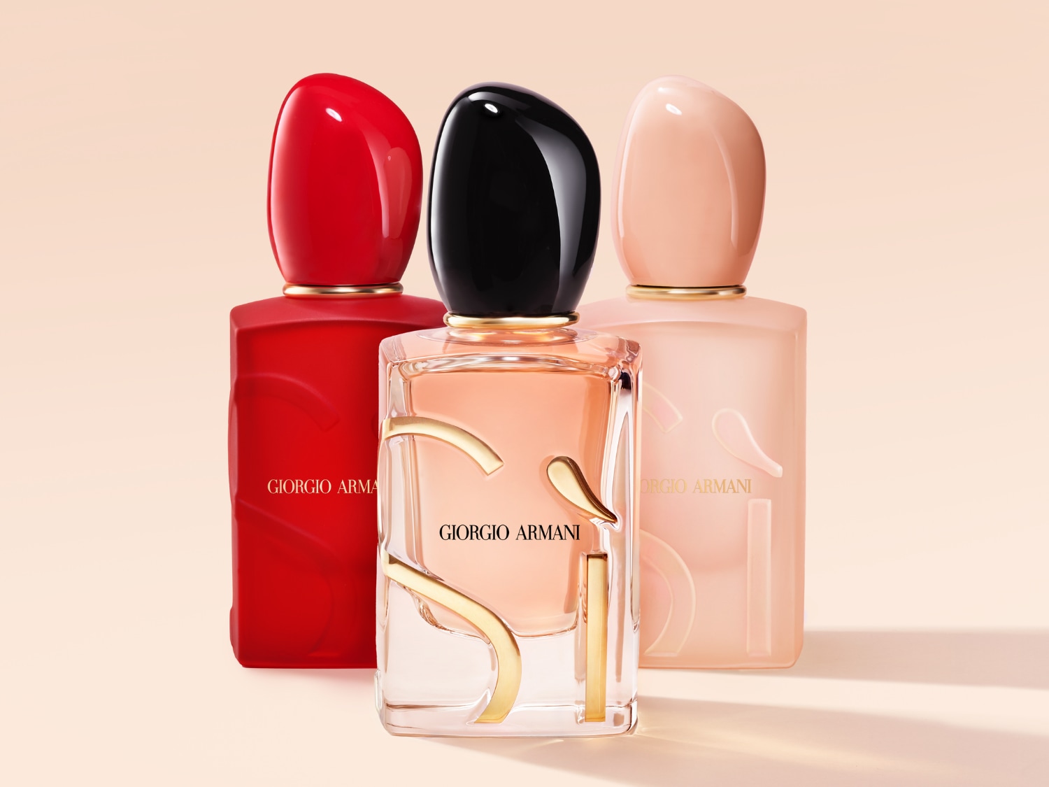 Tři flakony parfému Giorgio Armani v červené, černé a růžové barvě s hladkými, zaoblenými víčky a zlatými detaily.