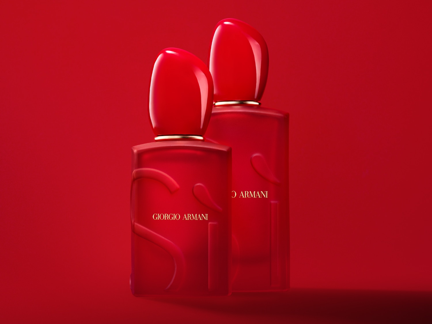 Dva červené flakony parfému Giorgio Armani Si stojí vedle sebe na červeném pozadí, s nápisem Giorgio Armani zlatým písmem.