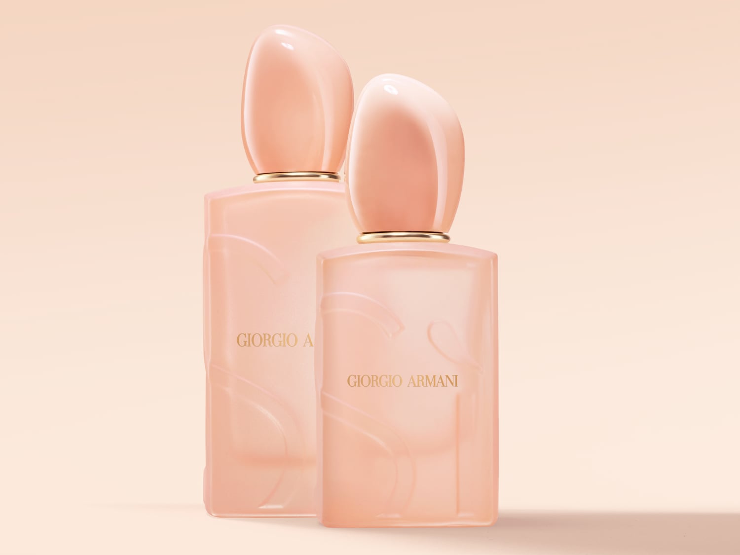 Dva flakony parfému Giorgio Armani v jemném růžovém odstínu s hladkým, zaobleným uzávěrem a zlatavým nápisem značky.