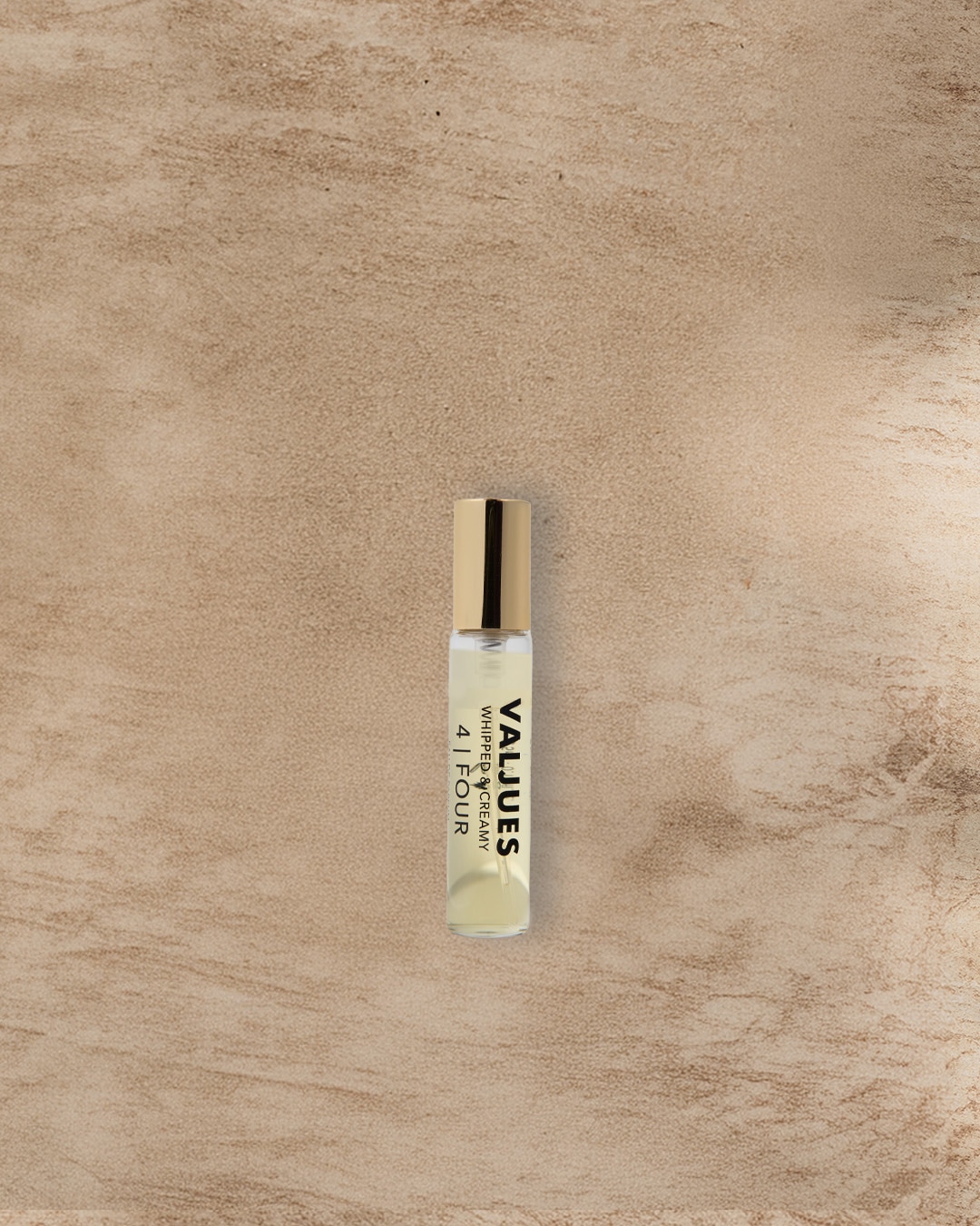 Eine durchsichtige Glasflasche mit goldener Kappe, gefüllt mit VALIUES Whipped & Creamy 4 | FOUR Flüssigkeit, steht auf einem beigen Untergrund.