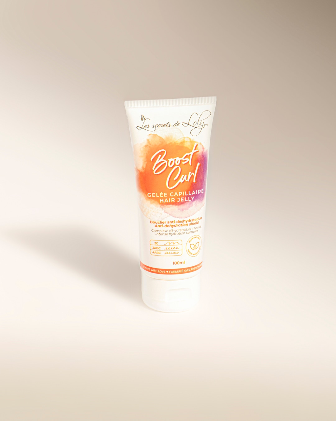 Le tube blanc de 100 ml de gelée capillaire Boost Curl de Les Secrets de Loly, avec une étiquette aux motifs aquarelle orange et violet, promet un bouclier anti-déshydratation et un complexe d'hydratation intense pour des boucles définies.