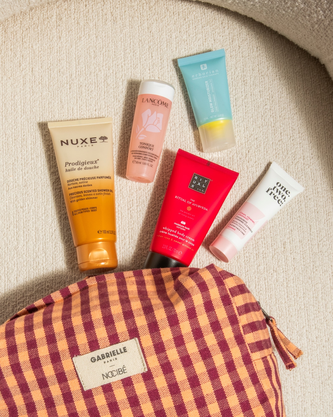 Découvrez un assortiment de produits de beauté essentiels, comprenant des soins pour le corps et le visage, présentés dans une trousse à carreaux Gabrielle Nocibé.