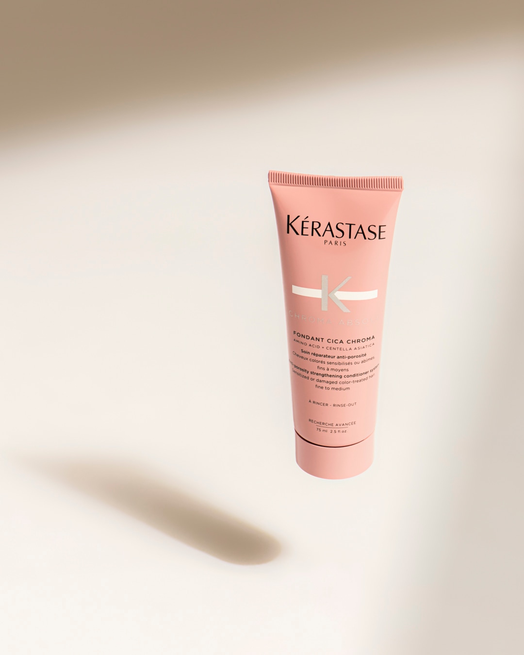 Le Fondant Cica Chroma de Kérastase, un après-shampooing rose pâle de 75 ml pour cheveux colorés et abîmés, enrichi en acides aminés et Centella Asiatica, est présenté sur un fond clair.