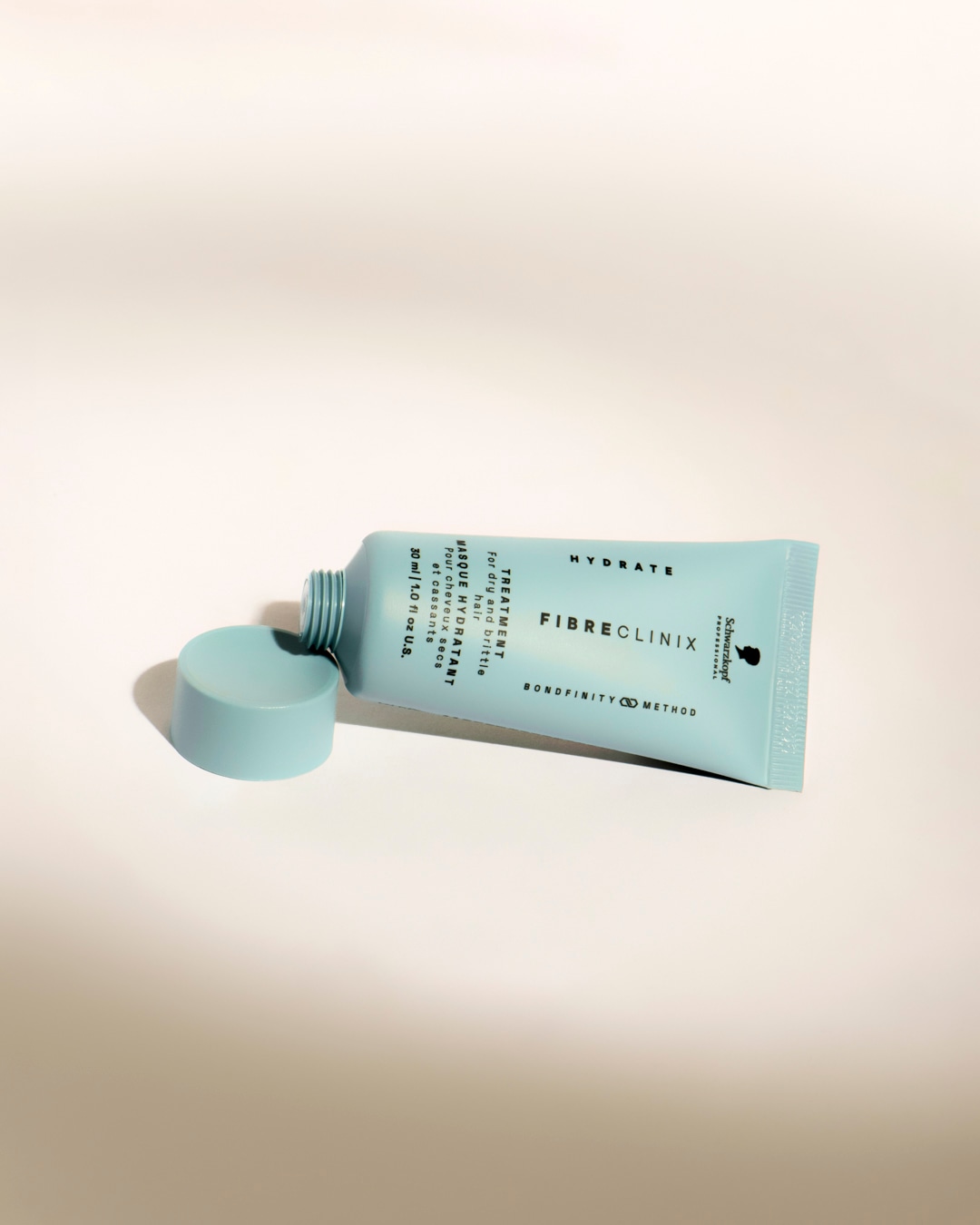 Le traitement hydratant Fibre Clinix de Schwarzkopf Professional, présenté dans un tube bleu clair de 30 ml avec son capuchon dévissé, est conçu pour les cheveux secs et cassants.