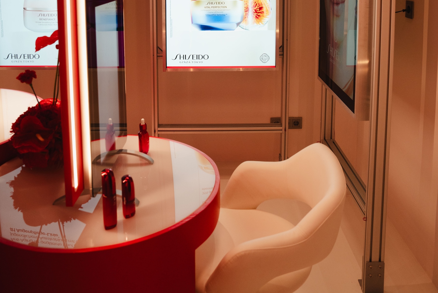 Einladender Shiseido-Counter mit roten Akzenten, der eine Auswahl an Hautpflegeprodukten auf einem eleganten, runden Tisch präsentiert, ergänzt durch einen bequemen Sessel.