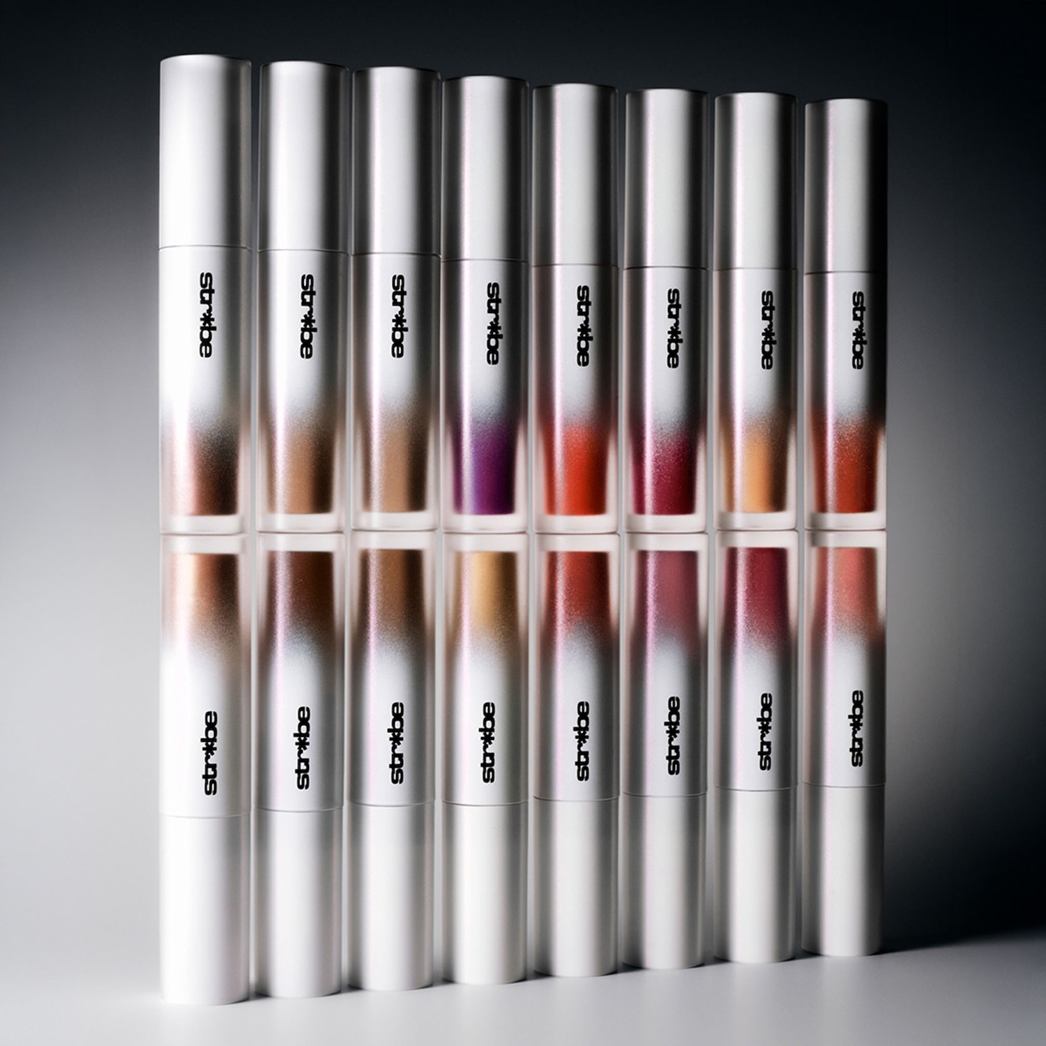 Een rij Stribe lipsticks in verschillende tinten, van bruin tot paars en rood, allemaal in strakke, zilveren verpakkingen.