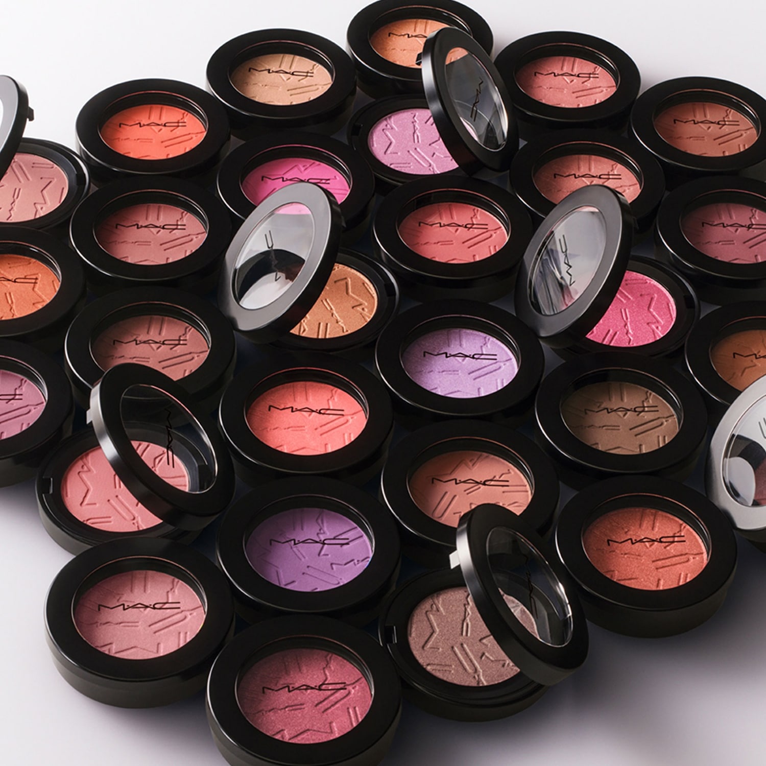 Een verzameling MAC blushes in verschillende tinten, van zachte perzik tot diep paars, elk in een zwarte compacte verpakking met het MAC logo.