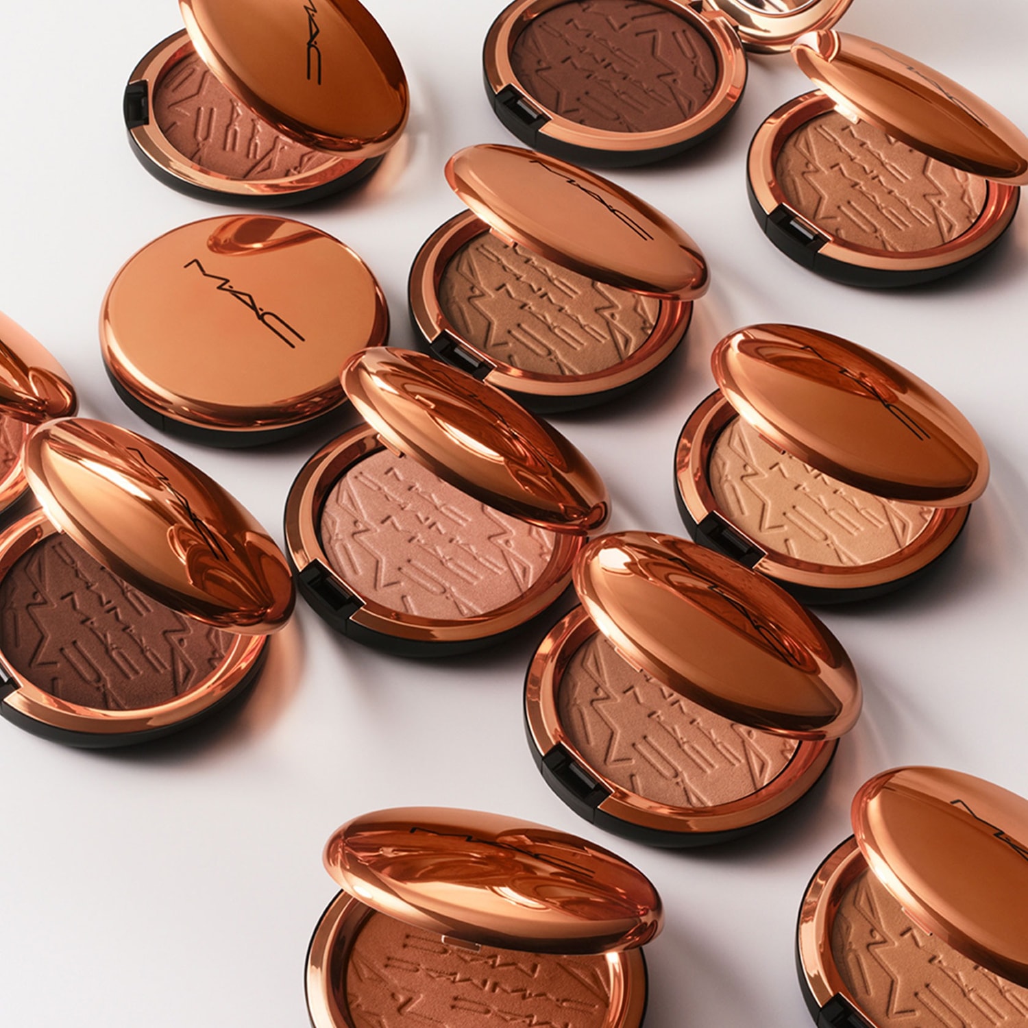 Een verzameling MAC-bronspoeders in glanzende, roségouden compacte verpakkingen met verschillende tinten en patronen.