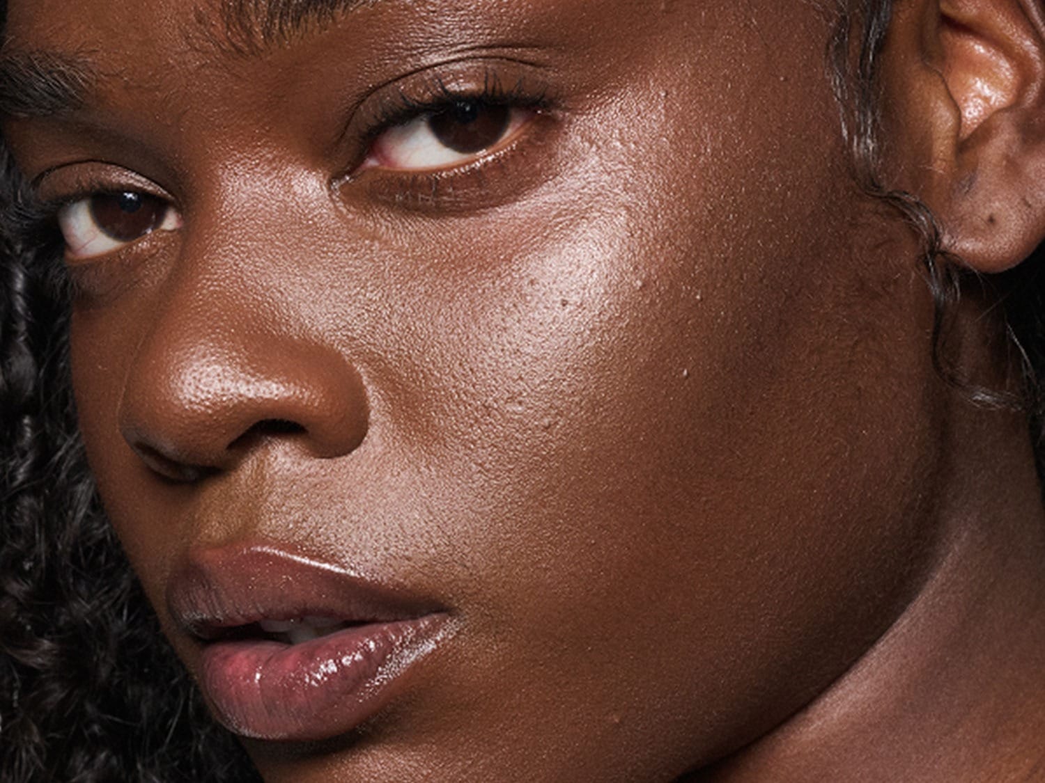 Close-up van een vrouw met een bruine huid, glanzende lippen en een natuurlijke make-up look.