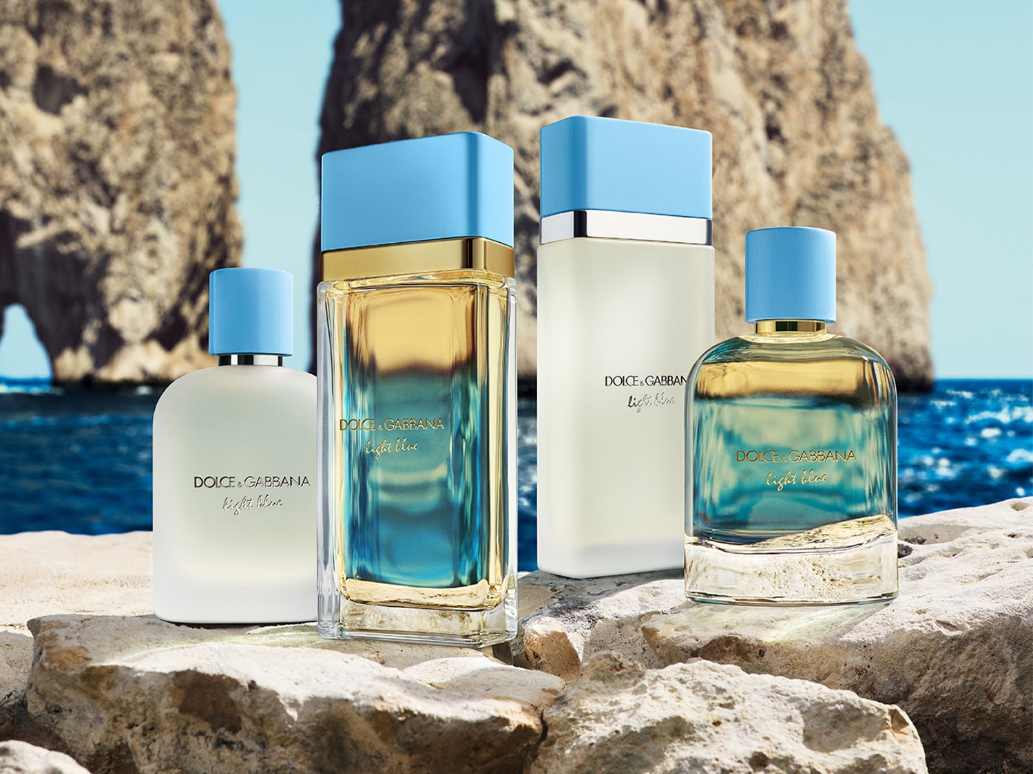 Quattro flaconi di profumo Dolce & Gabbana Light Blue con tappi azzurri su una superficie rocciosa, sullo sfondo il mare e le scogliere.