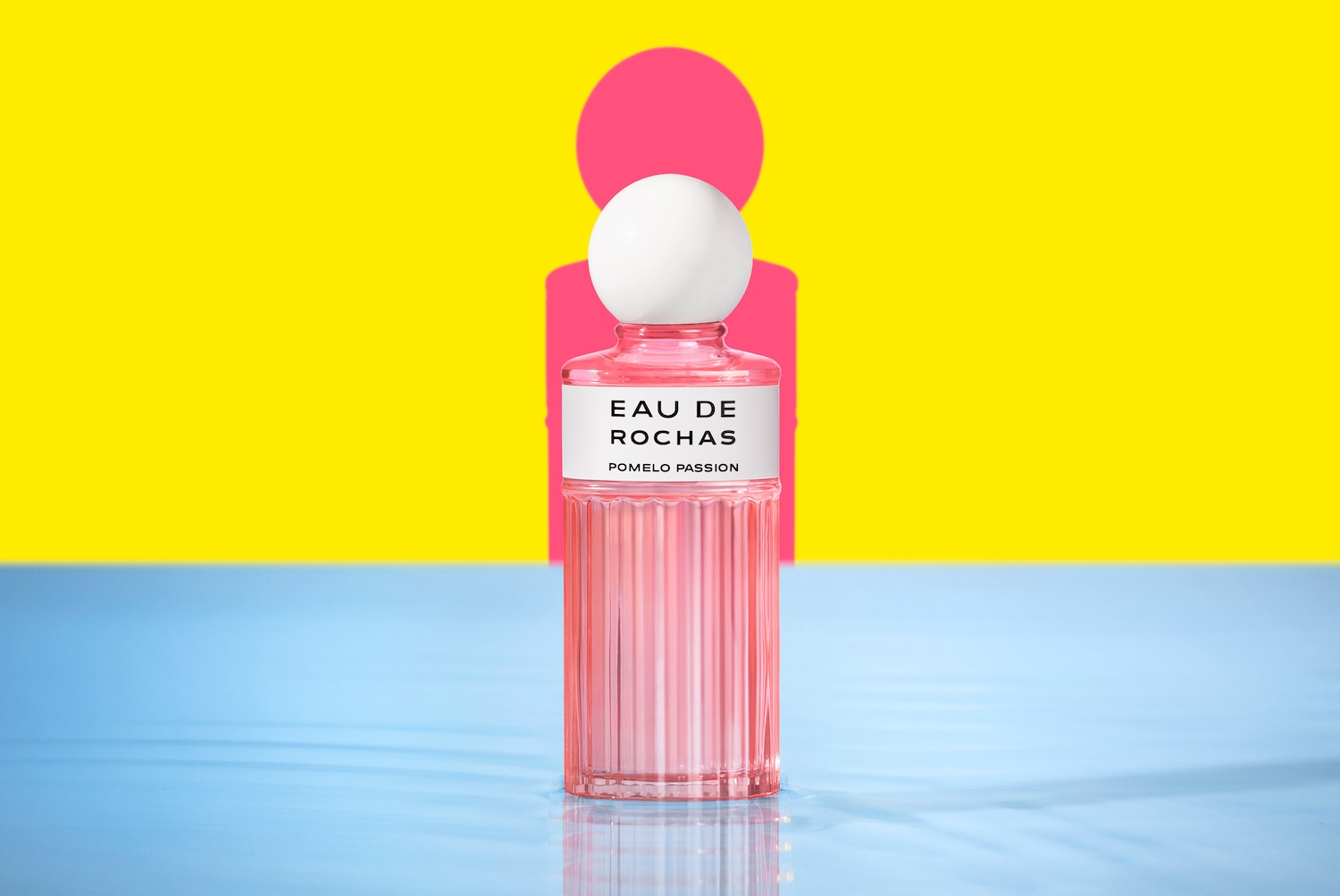 Voici Eau de Rochas Pomelo Passion, un parfum dans un flacon rose avec un bouchon blanc sphérique, sur un fond jaune et rose vif.