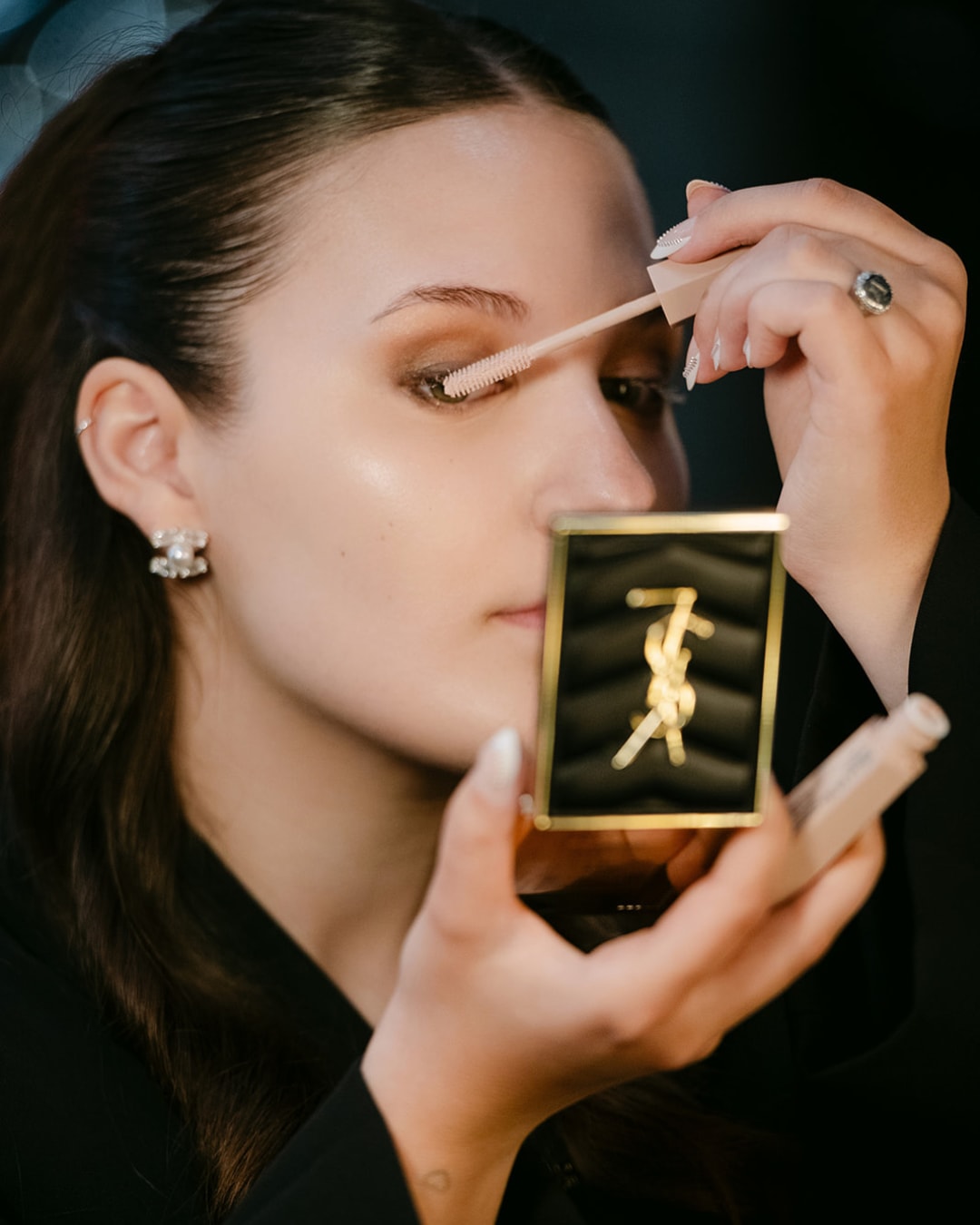 Een vrouw brengt mascara aan met een gouden YSL-compact in haar hand, voor een verfijnde oogopslag.