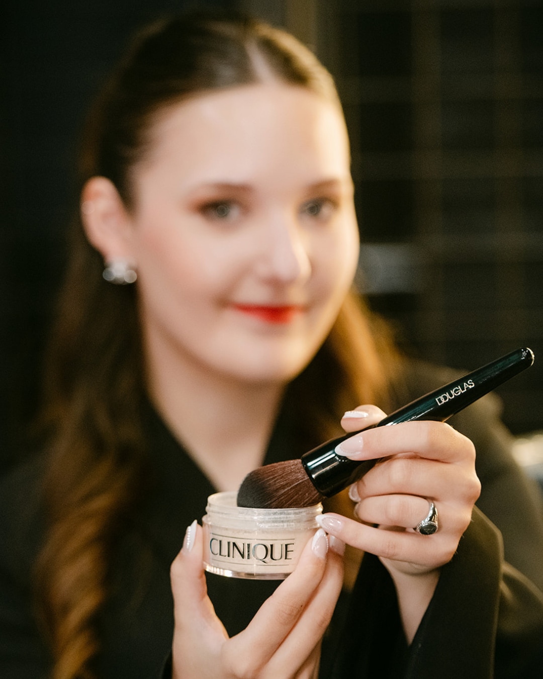 Een vrouw houdt een potje Clinique poeder vast met een Douglas make-up kwast, klaar om de perfecte finishing touch aan te brengen.