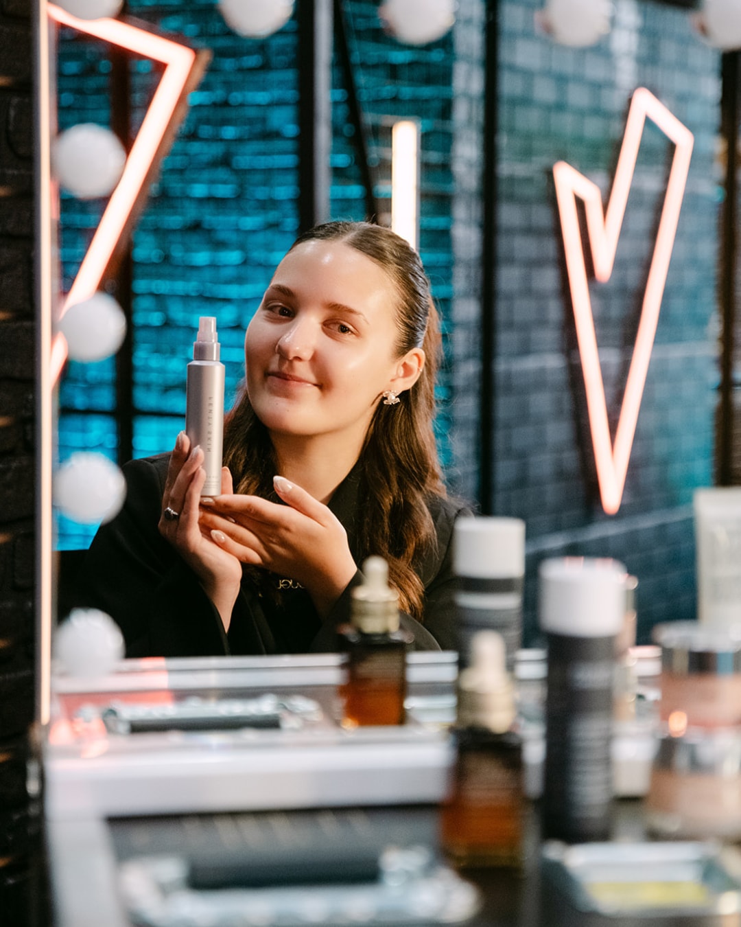 Een jonge vrouw houdt een zilverkleurige fles REN Clean Skincare vast, met een glimlach en een blik van vertrouwen.