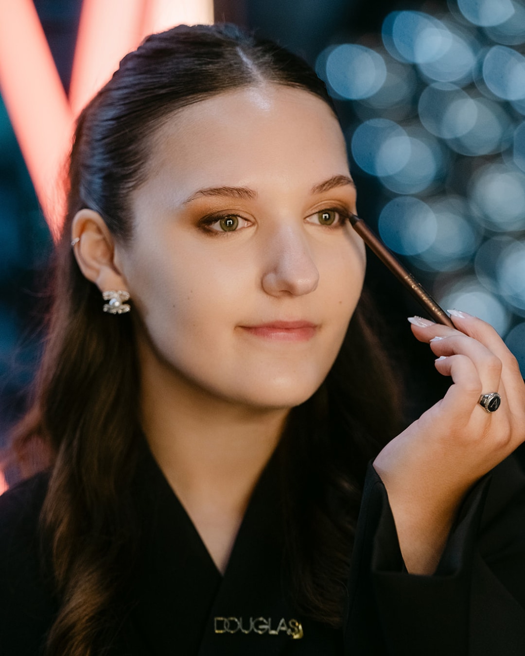 Een jonge vrouw met bruin haar en een zwarte jas brengt bruine eyeliner aan op haar ooglid voor een subtiele, verfijnde look.