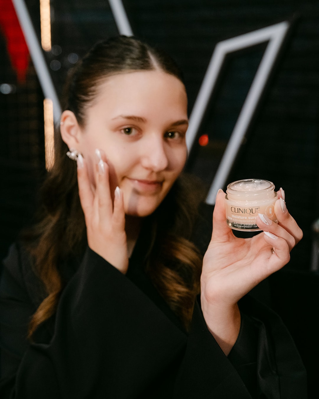 Een vrouw houdt een potje Clinique Moisture Surge vast, een hydraterende crème voor een stralende huid.