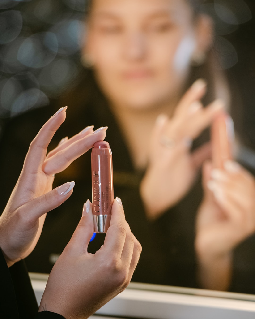 Een vrouw houdt een Clinique Chubby Stick tint in de kleur 'Super Quick Earth' vast, klaar om haar lippen te accentueren met een vleugje kleur.