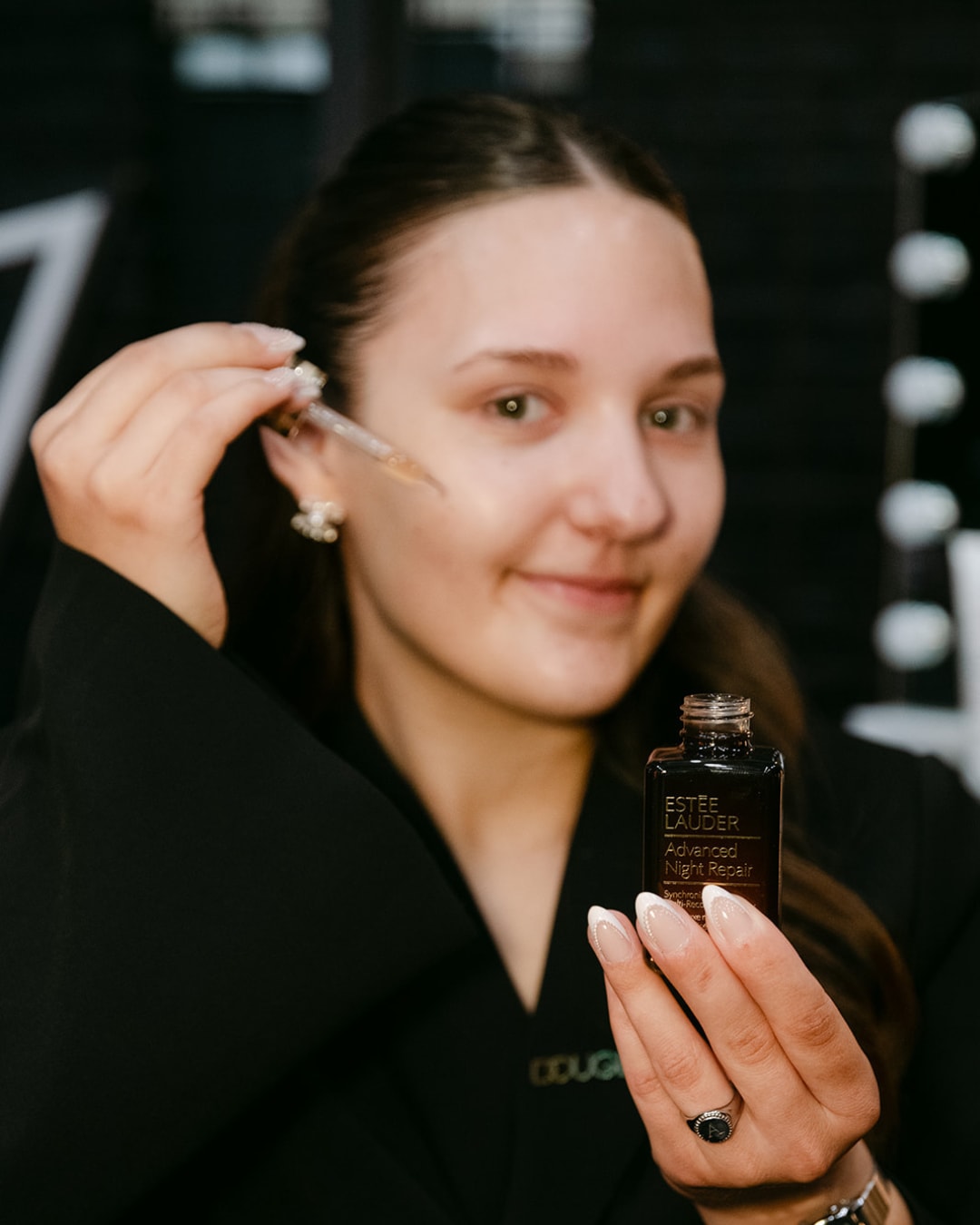 Een vrouw gebruikt Estée Lauder Advanced Night Repair serum met een pipet, de verpakking is donkerbruin met witte letters.