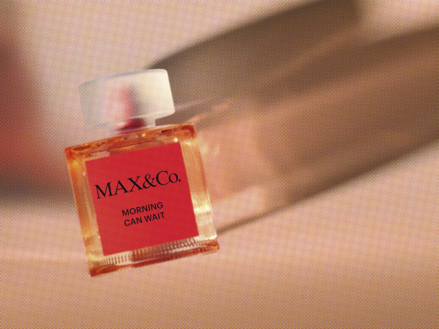 Butelka perfum Max&Co. Morning Can Wait ma kwadratowy kształt z czerwoną etykietą i przezroczystą nakrętką, emanuje nowoczesną elegancją.