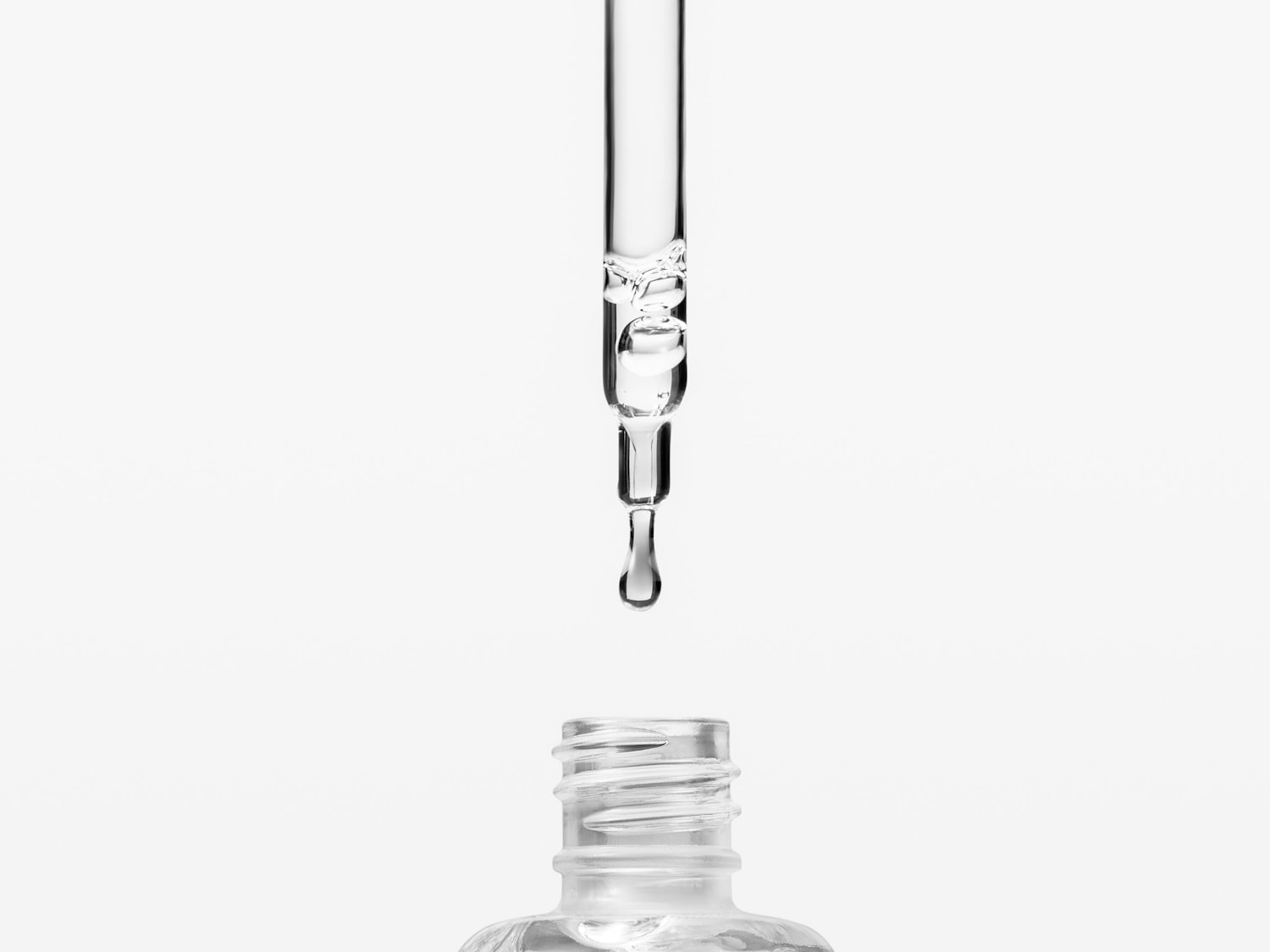 Picătură limpede căzând dintr-o pipetă transparentă într-o sticlă, sugerând un ser sau ulei esențial pentru îngrijirea pielii.
