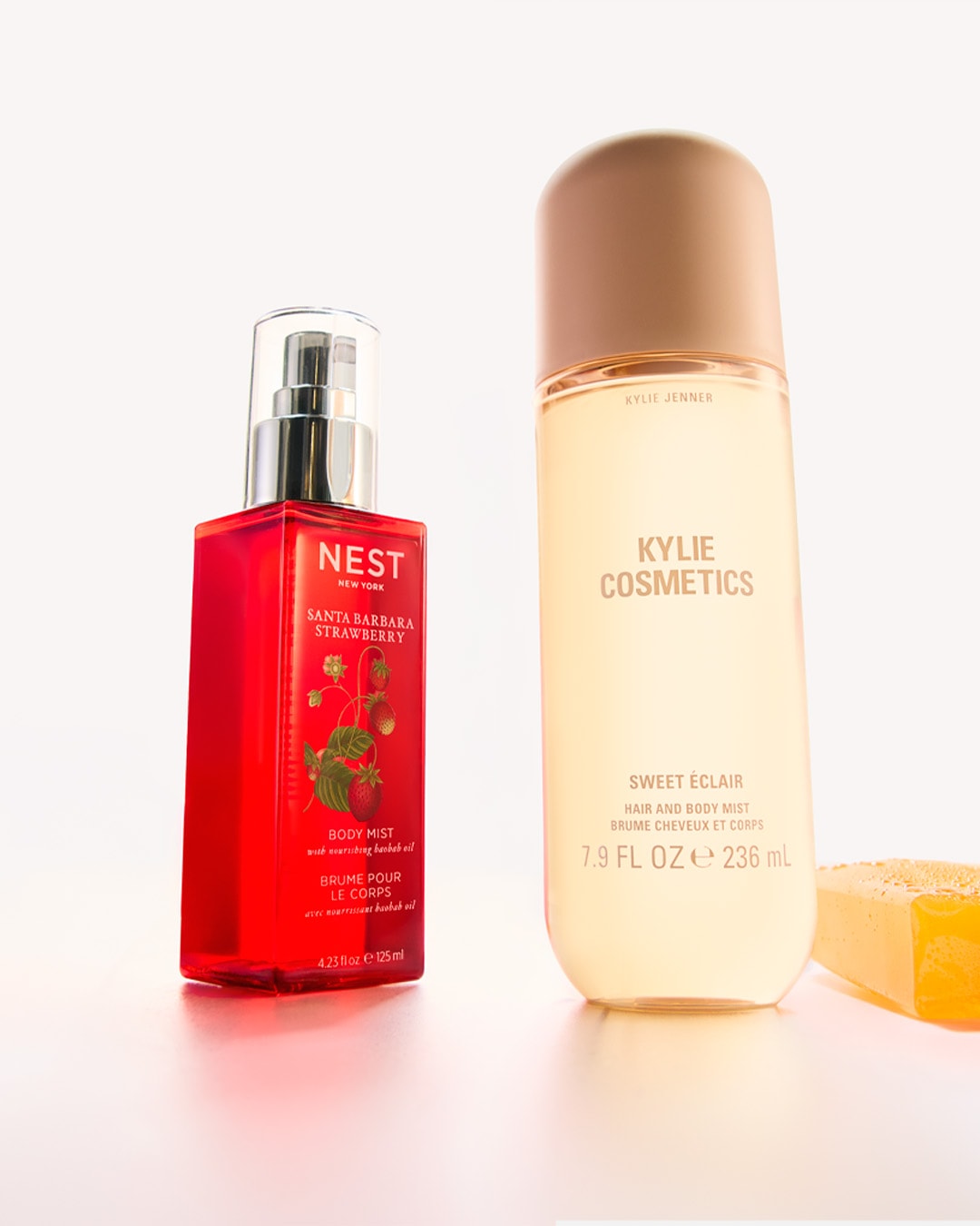 Twee flessen body mist, één van Nest New York in een rode fles met aardbeienafbeeldingen, en één van Kylie Cosmetics in een beige fles, beide voor haar en lichaam.