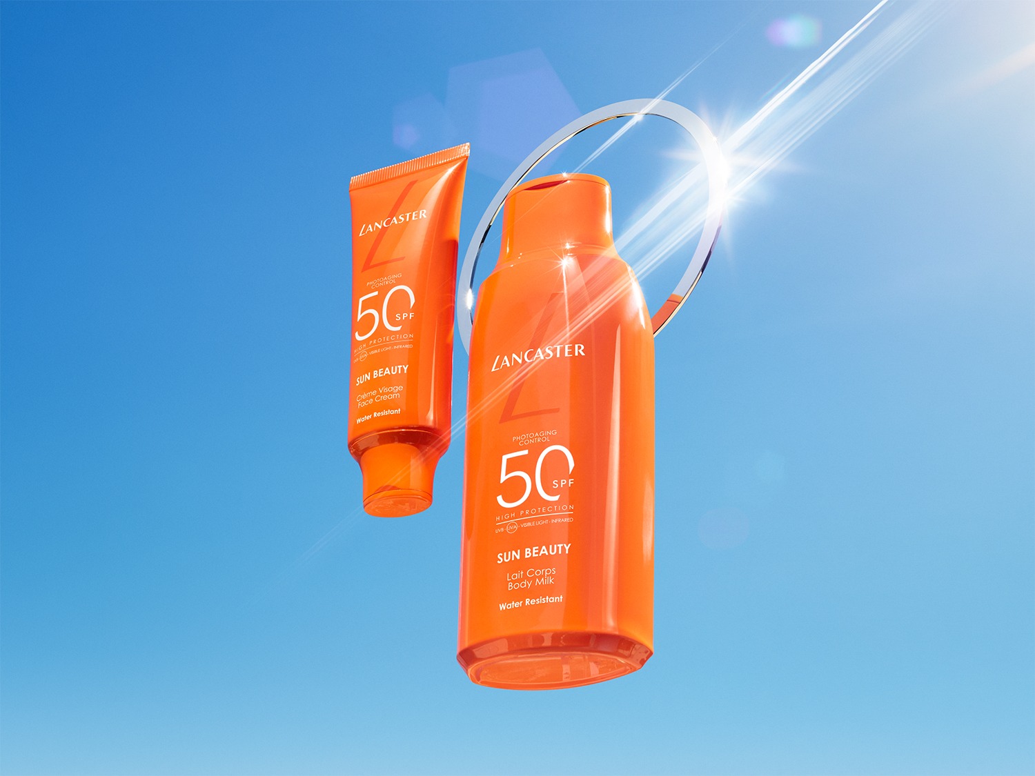 Twee oranje Lancaster zonnebrandproducten, een gezichtscrème en een bodymilk, staan tegen een helderblauwe lucht met een zilveren ring en zonnestralen.