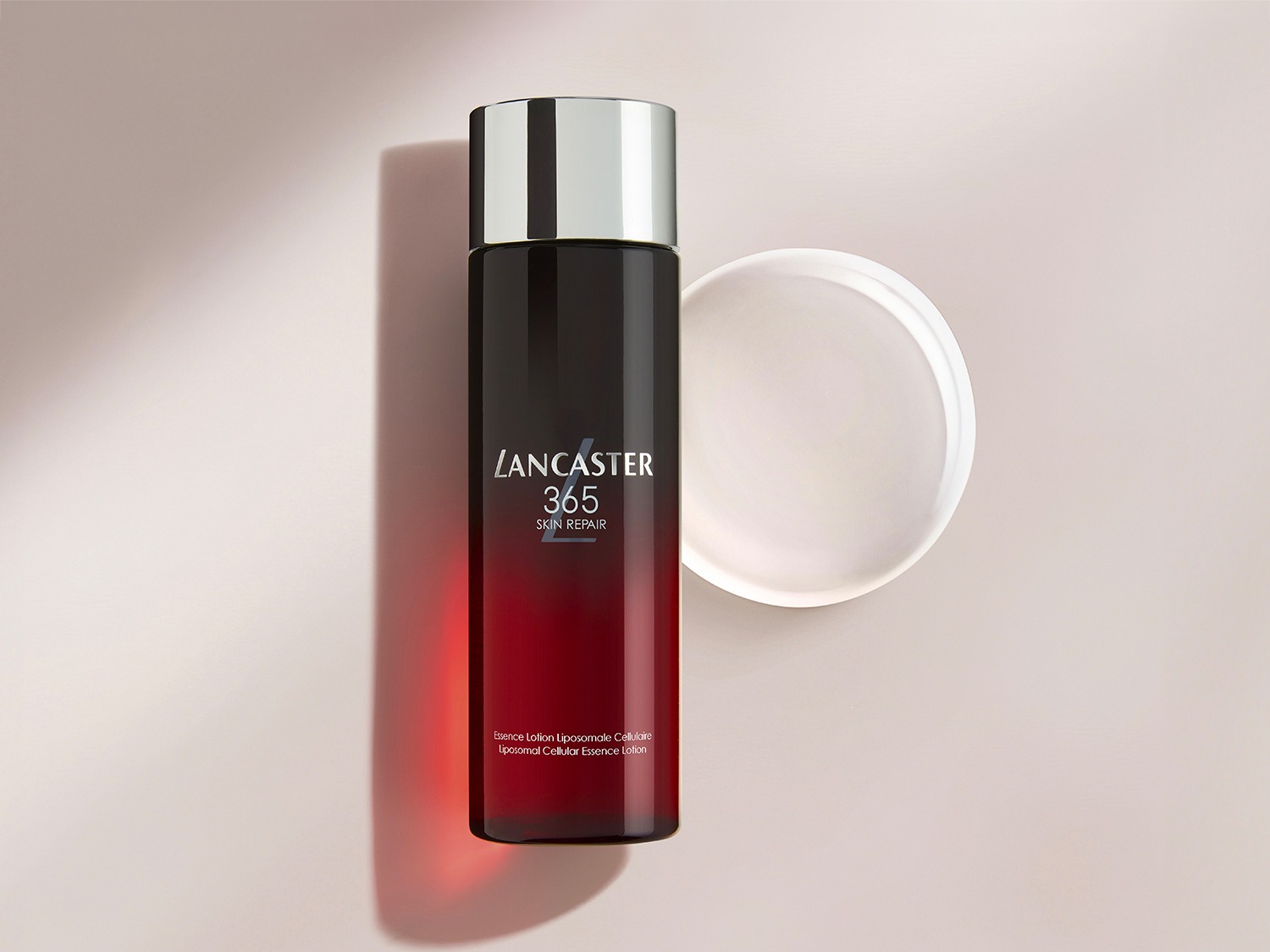 Ontdek Lancaster 365 Skin Repair Essence Lotion in een elegante, zwart-rood verlopende flacon met zilveren dop, voor een cellulaire herstellende werking.