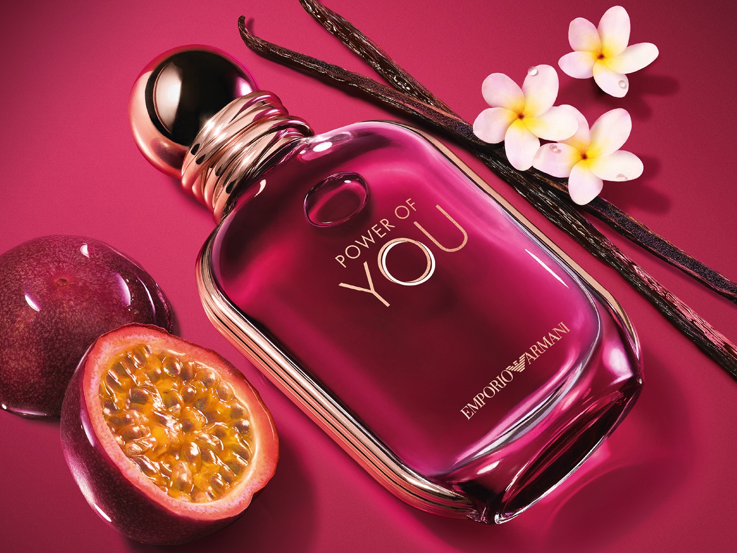 Een close-up van een roze Emporio Armani parfumfles 'Power of You', vergezeld van passievruchten, vanillestokjes en witte bloemen.