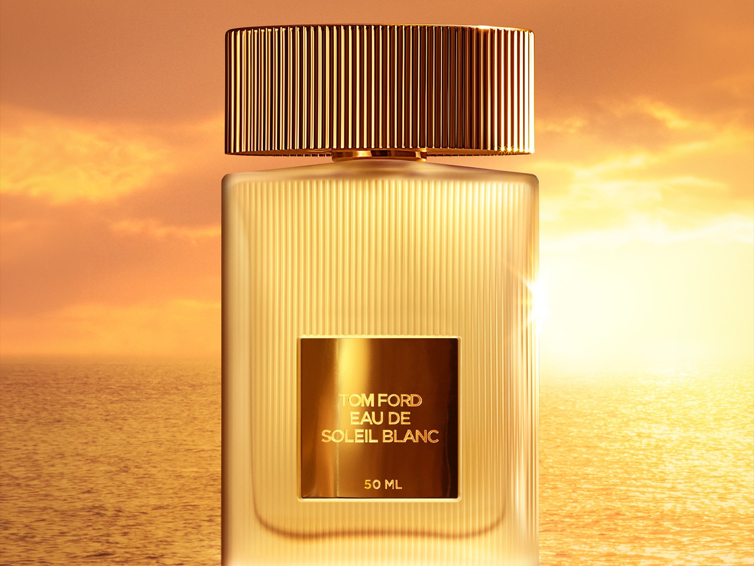 Nahaufname von Tom Ford Eau de Soleil Blanc in einem matten transparenten Flakon mit goldenem Etikett und Verschluss; im Hintergrund ein malerischer Sonnenaufgang über dem Meer.