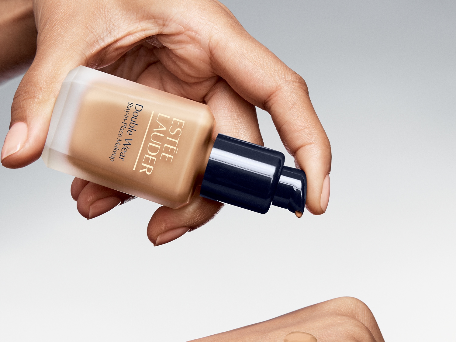 Detailní pohled na make-up Estée Lauder Double Wear Stay-in-Place v průhledné skleněné lahvičce s pumpičkou, který je aplikován na pokožku.