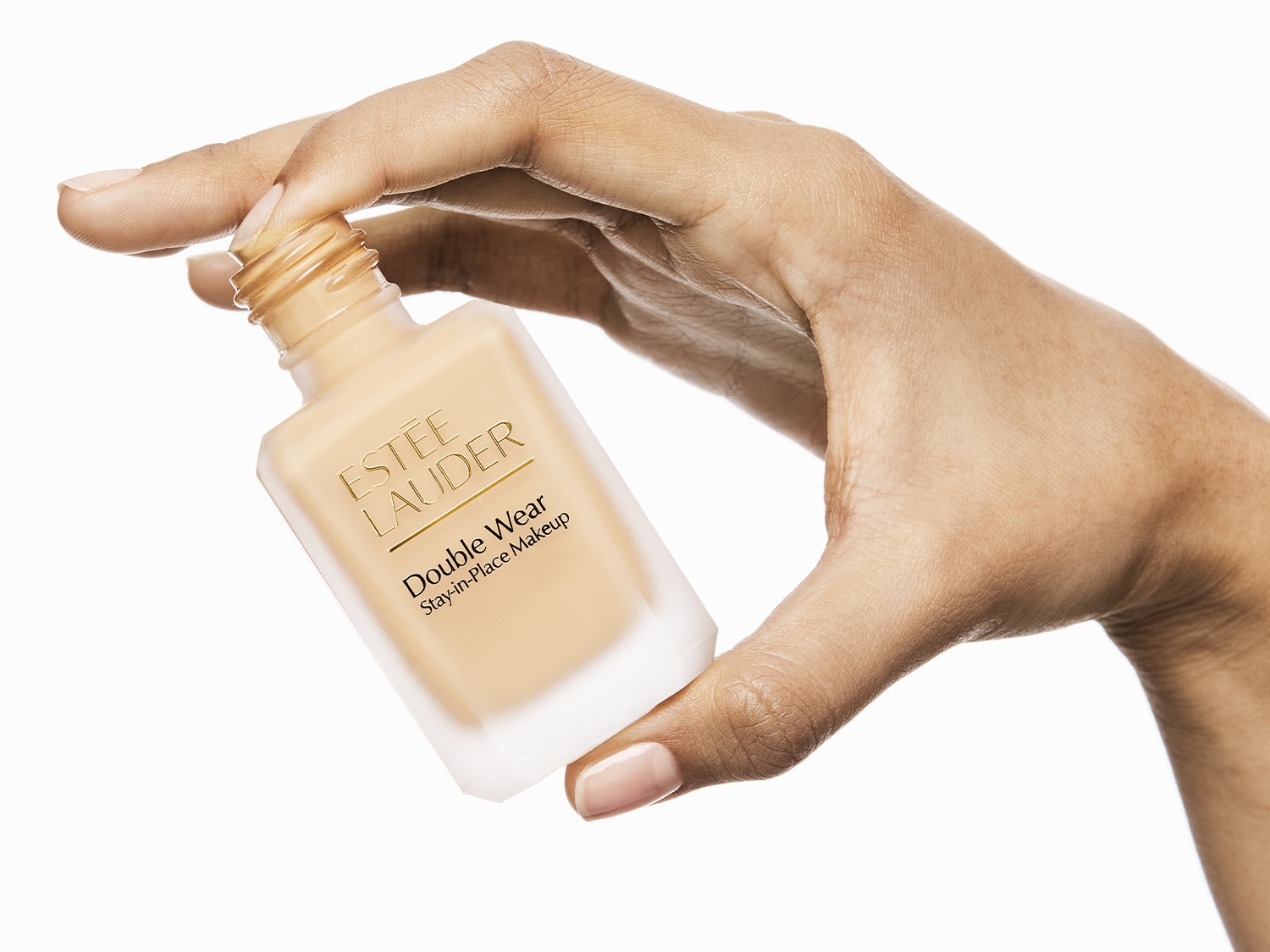 Detailní pohled na make-up Estée Lauder Double Wear Stay-in-Place v průhledné skleněné lahvičce držené v ruce, ideální pro dlouhotrvající dokonalý vzhled.