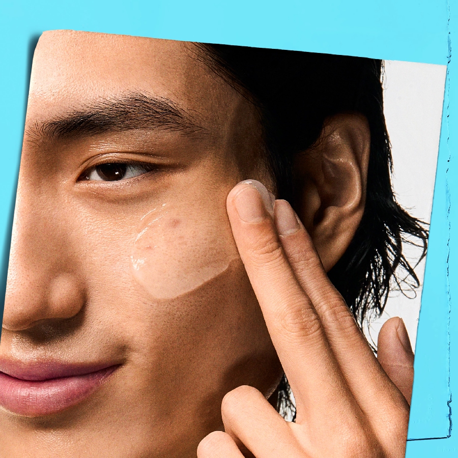 Un homme asiatique applique un sérum transparent sur sa joue, soulignant une routine de soin pour une peau éclatante.