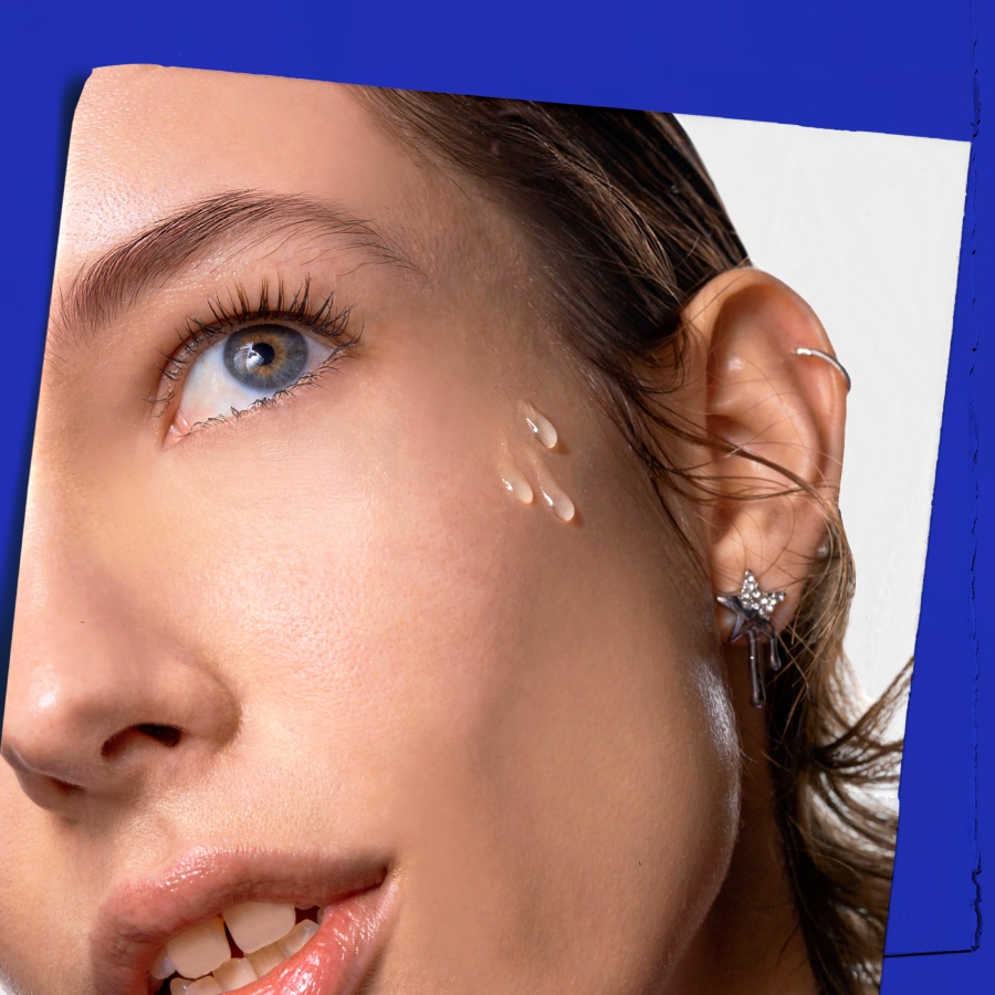 Gros plan sur le visage d'une femme avec des gouttes de sérum transparent sur la joue, mettant en valeur une peau hydratée et éclatante.