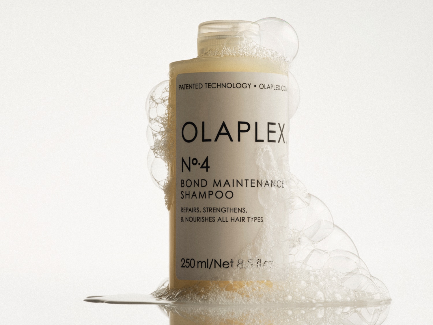 Olaplex No.4 Bond Maintenance Shampoo in een witte fles omringd door zeepbellen, die het haar herstelt, versterkt en voedt.