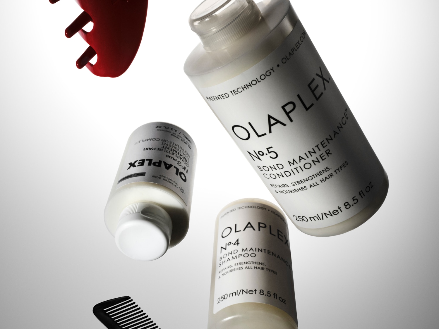 Olaplex No.3 Plus haarreparatie, No.5 conditioner en No.4 shampoo in witte flessen, samen met een rode en zwarte kam, voor het herstellen, versterken en voeden van alle haartypes.