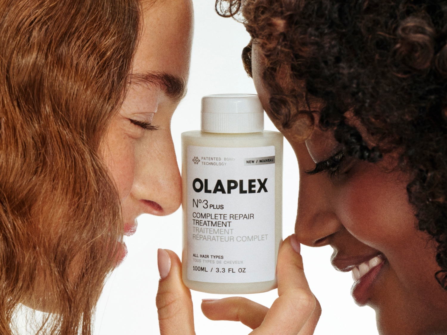 Twee mensen met verschillende haartypes houden een witte fles Olaplex Nº3 PLUS Complete Repair Treatment vast, een haarbehandeling voor alle haartypes.