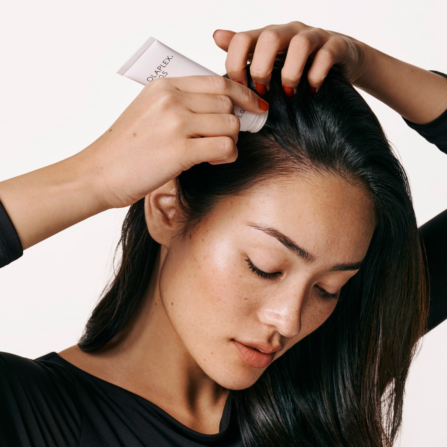 Een vrouw met lang, donker haar brengt Olaplex No. 0 aan op haar hoofdhuid met een witte tube.