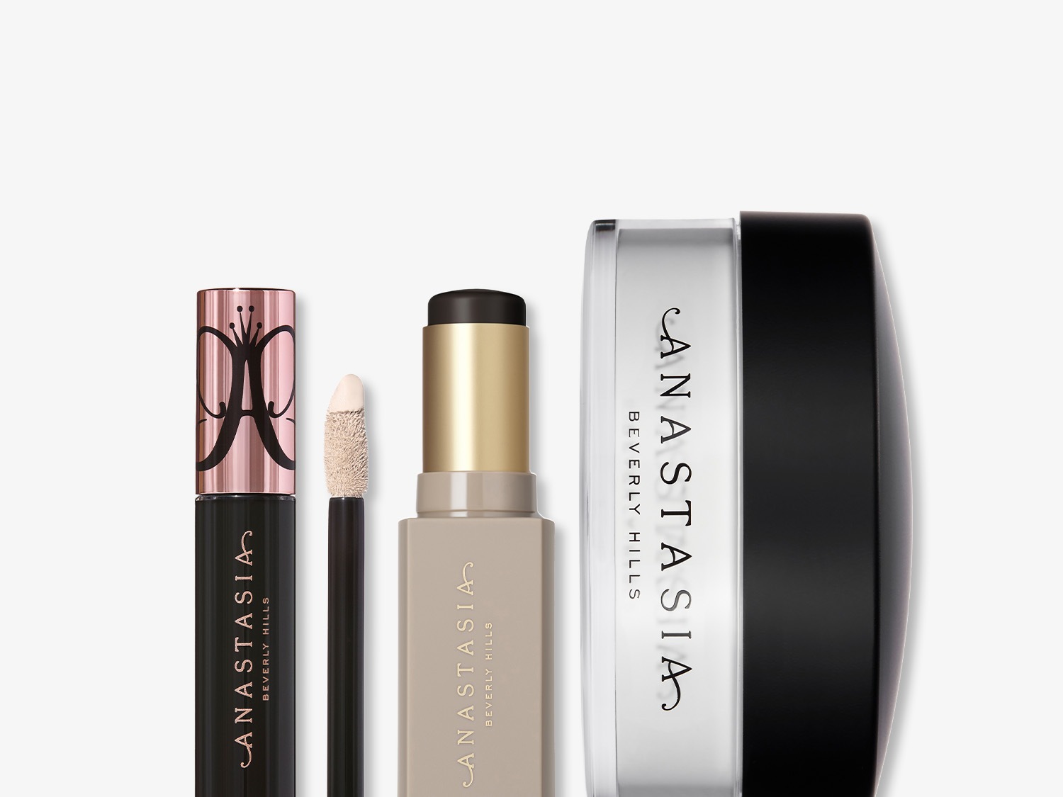 Kolekcja kosmetyków Anastasia Beverly Hills obejmuje korektor w płynie z aplikatorem, sztyft do konturowania w beżowym opakowaniu i puder w przezroczystym słoiczku z czarną zakrętką.