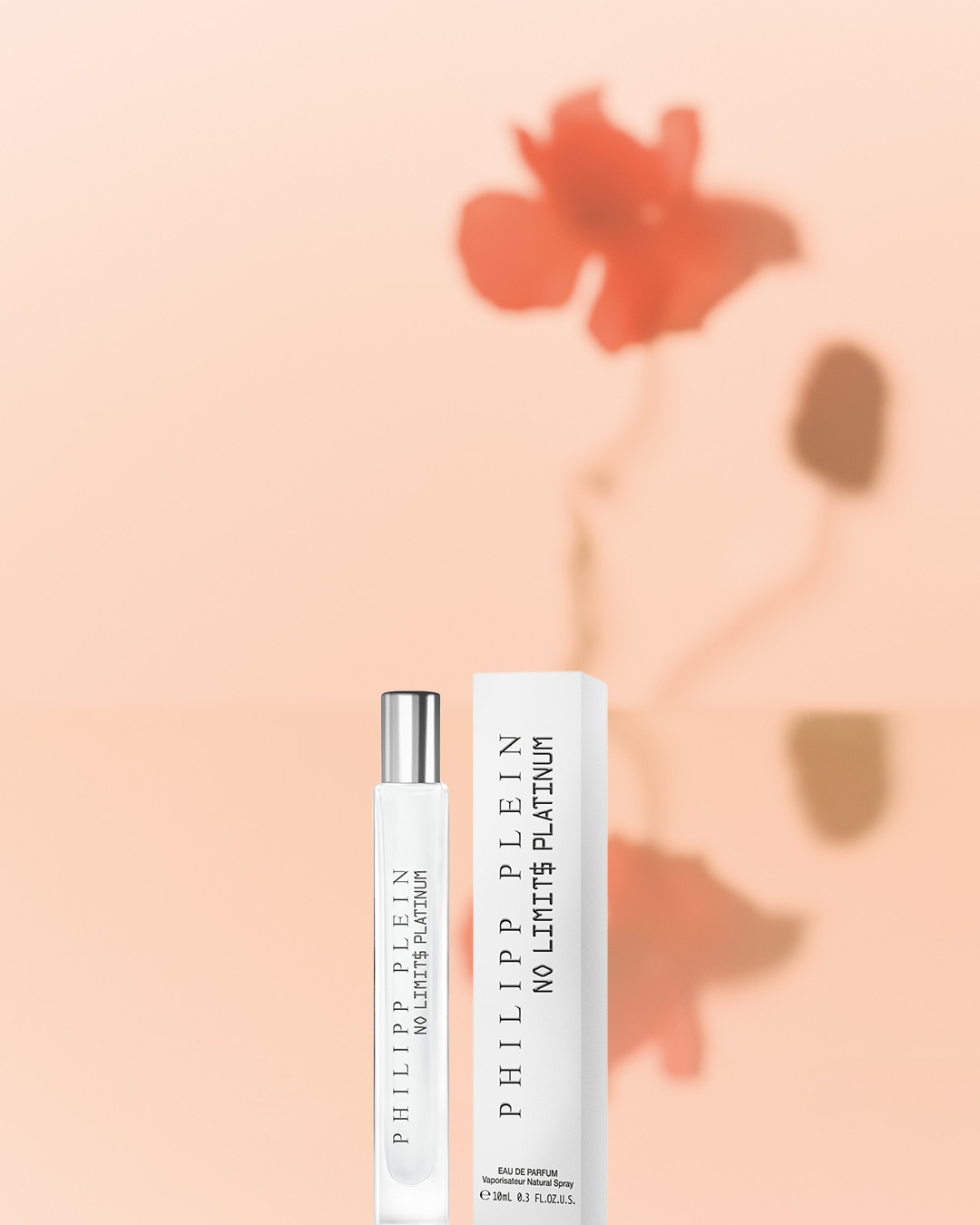 Biały flakon perfum Philipp Plein No Limits Platinum o pojemności 10 ml, z srebrną zatyczką, stoi obok białego pudełka z nazwą perfum na tle delikatnej, brzoskwiniowej poświaty.