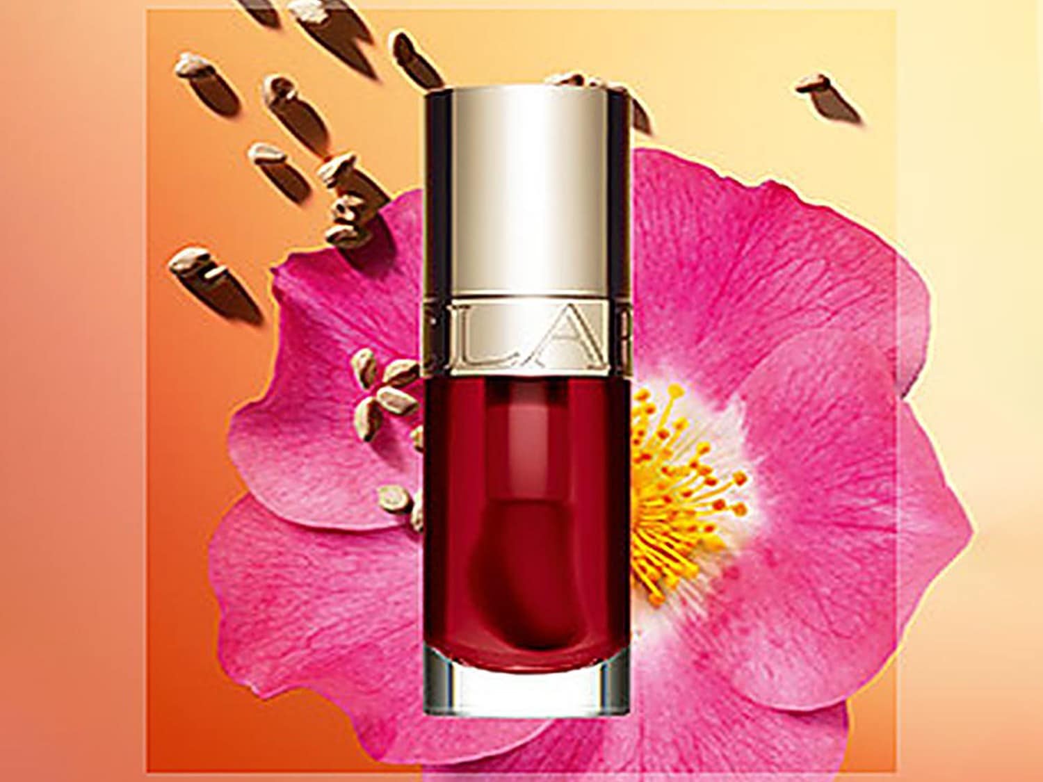 Uleiul pentru buze Clarins are o nuanță roșie intensă, ambalat într-un recipient elegant, cu capac argintiu, așezat lângă o floare roz vibrantă.