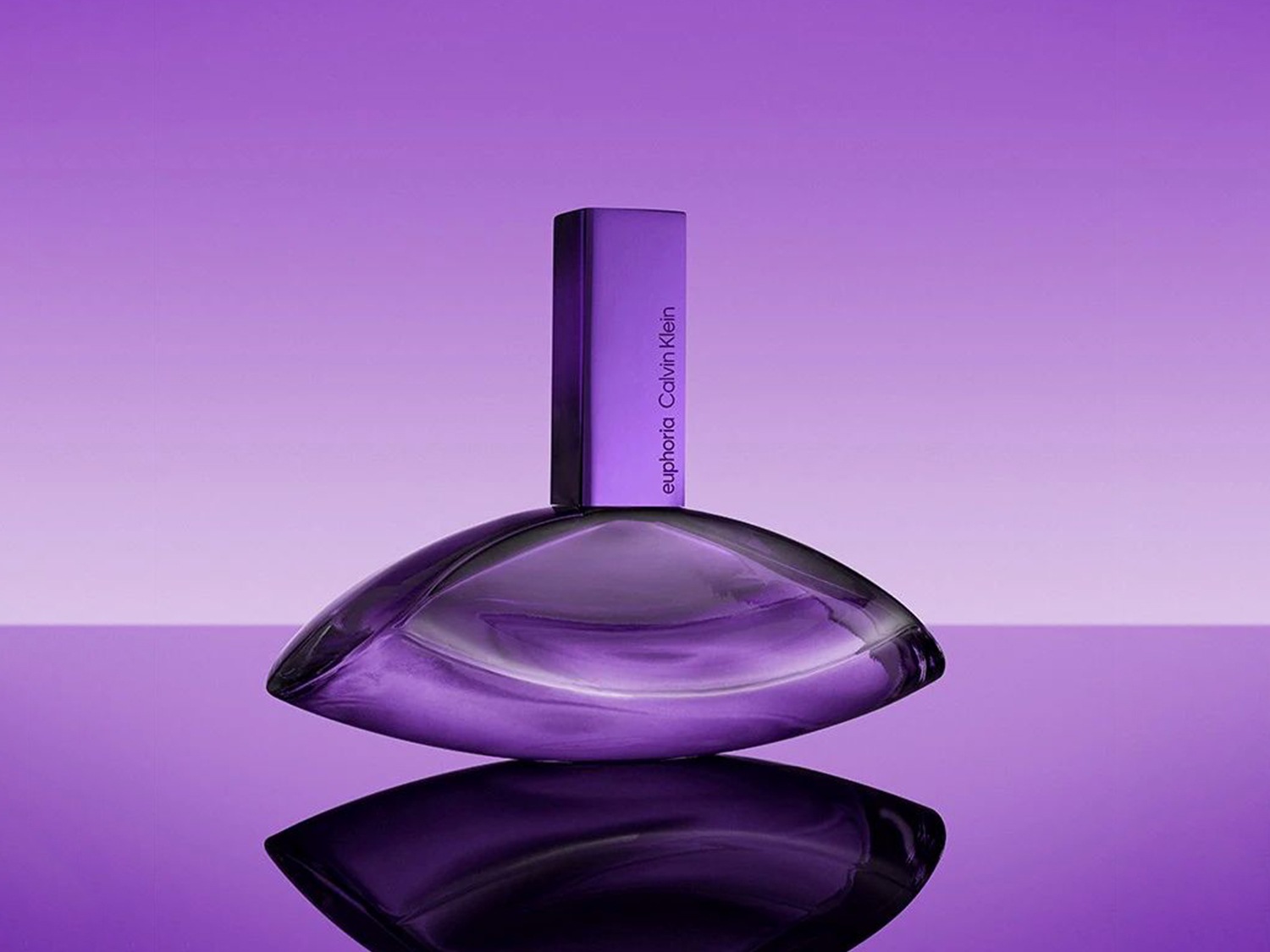 Sticla de parfum Calvin Klein Euphoria are o formă organică, violetă, cu un capac dreptunghiular și o etichetă subtilă, reflectată pe o suprafață lucioasă, totul pe un fundal violet gradient.