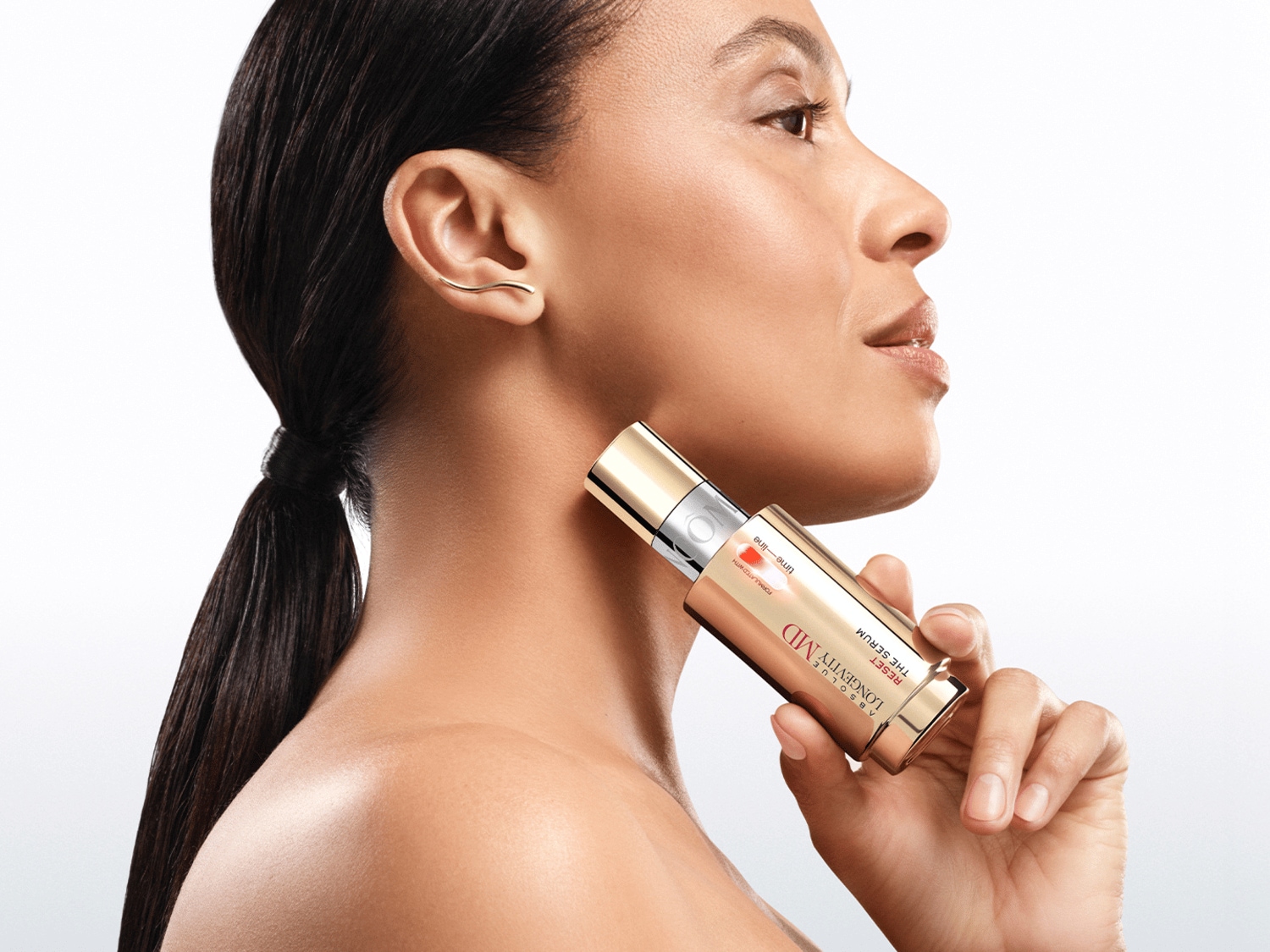 Profil ženy, která si na krk nanáší sérum Absolute Longevity MD Reset The Serum ve zlatém obalu.