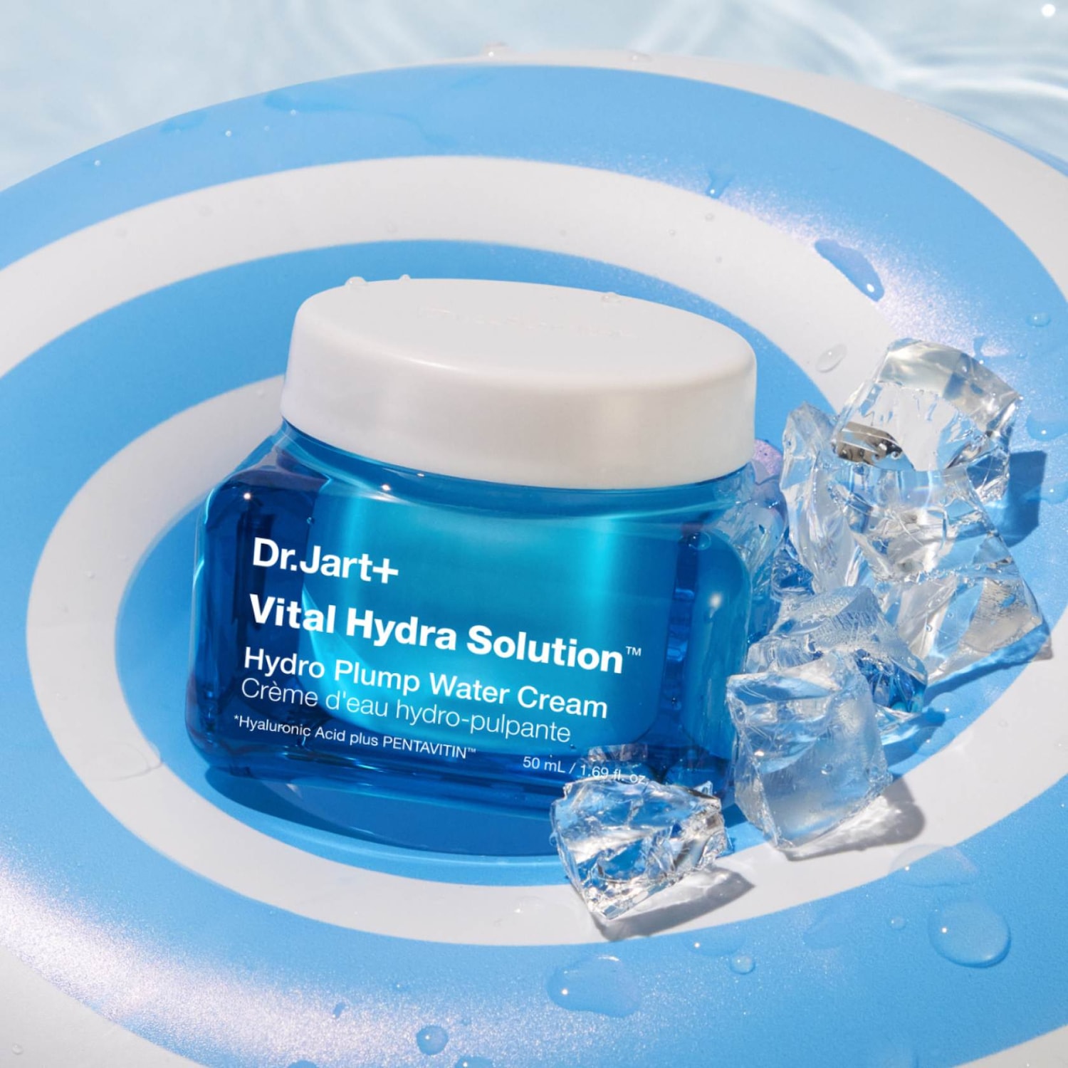 Niebieski krem Dr.Jart+ Vital Hydra Solution Hydro Plump Water Cream w przezroczystym słoiczku z białą nakrętką, otoczony kostkami lodu i umieszczony na dmuchanym kole w biało-niebieskie paski.
