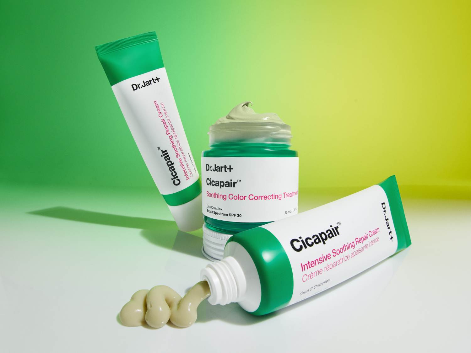Zdjęcie przedstawia trzy produkty Dr.Jart+ Cicapair: krem w tubce, krem w słoiczku i wyciśniętą porcję kremu o jasnobeżowym odcieniu.