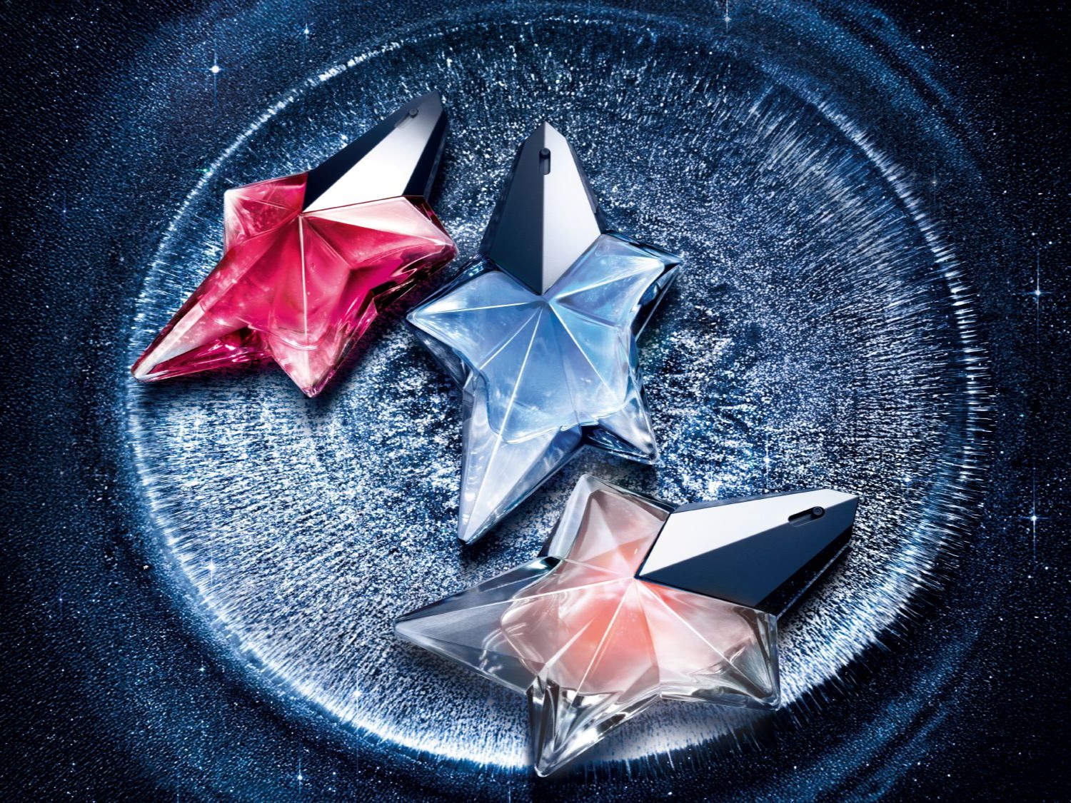 Découvrez un trio de parfums Angel de Mugler, chacun dans un flacon en forme d'étoile aux teintes rose, bleu et pêche, sur un fond bleu scintillant évoquant une nuit étoilée.