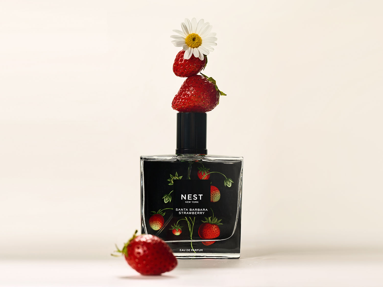 Flakon perfum Nest New York Santa Barbara Strawberry z czarną etykietą ozdobioną motywem truskawek, na korku ułożone dwie truskawki i stokrotka, a obok leży truskawka.