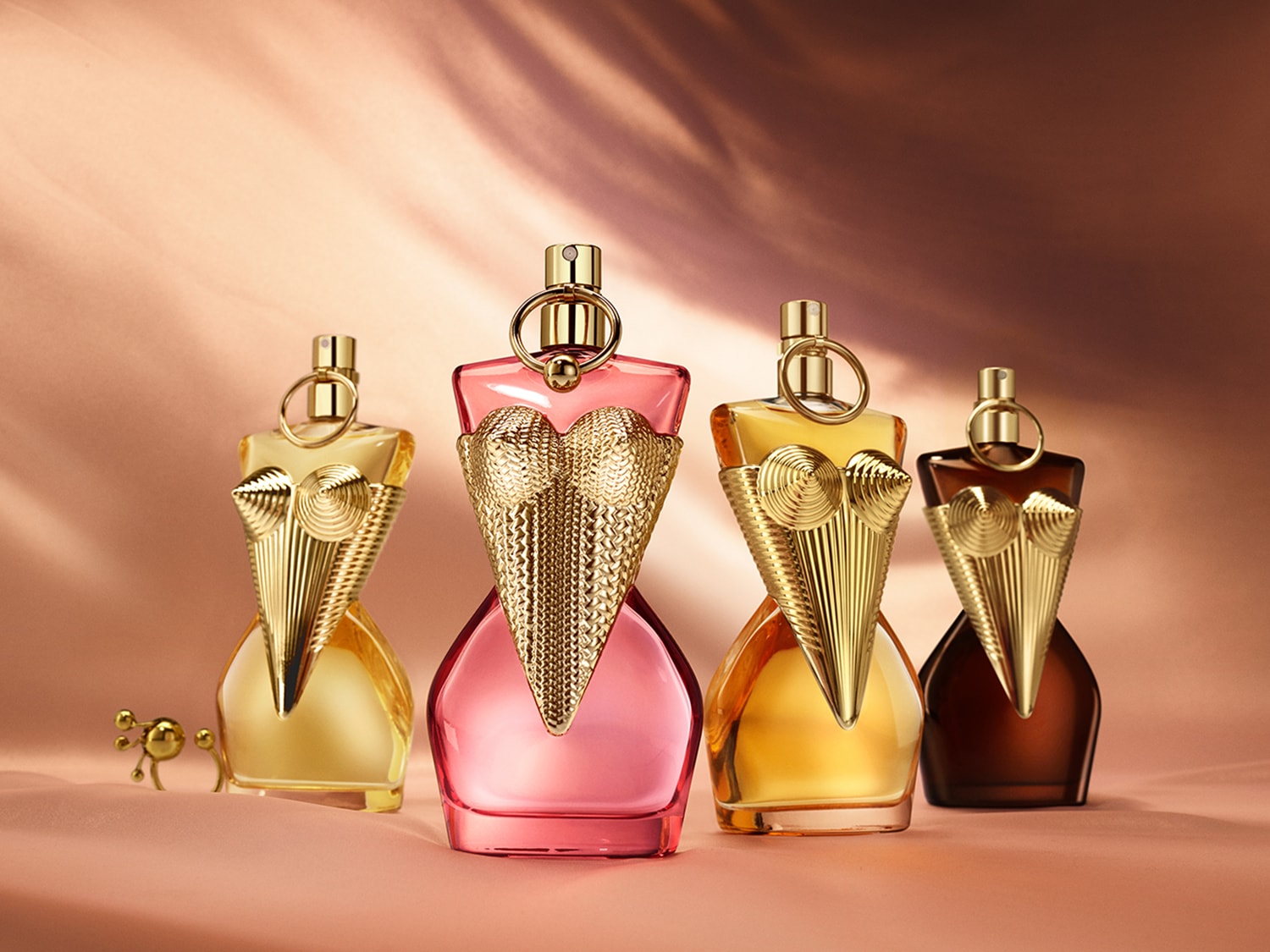 Vier Parfümflakons in Form eines weiblichen Torsos, gefüllt mit Flüssigkeiten in den Farben Gold, Rosa, Bernstein und Dunkelbraun, stehen nebeneinander und präsentieren sich in einem eleganten Licht.