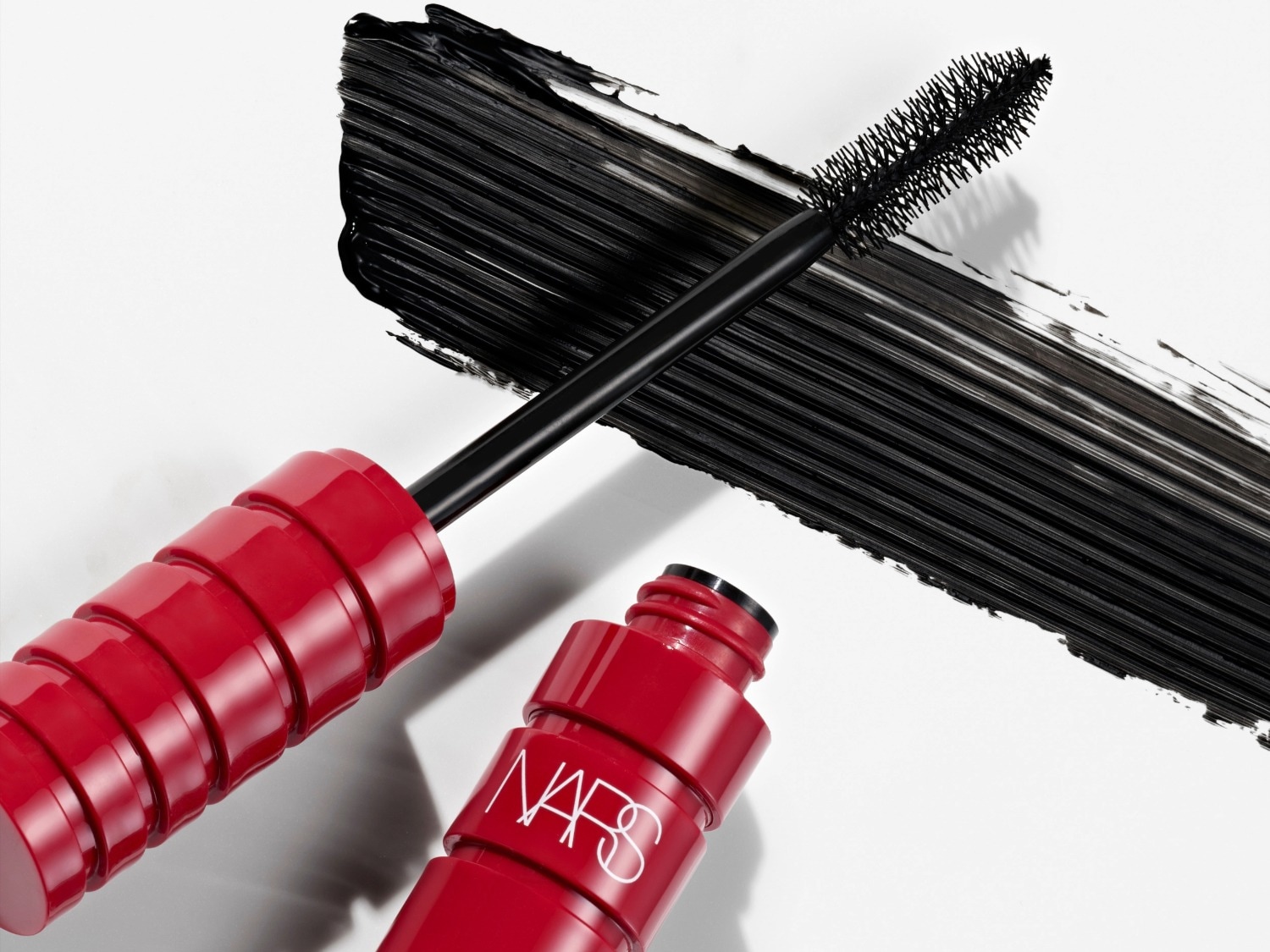 Mascara NARS rouge vif avec une brosse noire et un trait épais de mascara noir sur fond blanc, pour des cils spectaculaires.