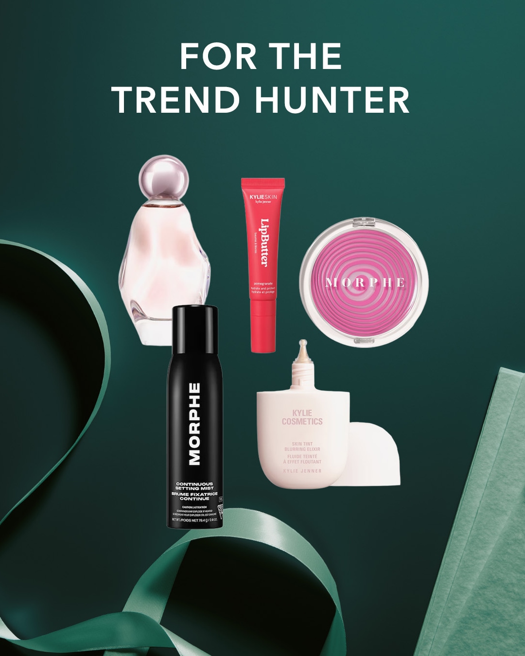 Entdecken Sie die Must-haves für Trendsetter: ein zartrosa Parfümflakon, ein roter Kylie Skin Lip Butter, ein pinkes Morphe Rouge, ein schwarzes Morphe Continuous Setting Mist und ein beiger Kylie Cosmetics Skin Tint Blurring Elixir, alles vor einem dunkelgrünen Hintergrund mit einem grünen Band.
